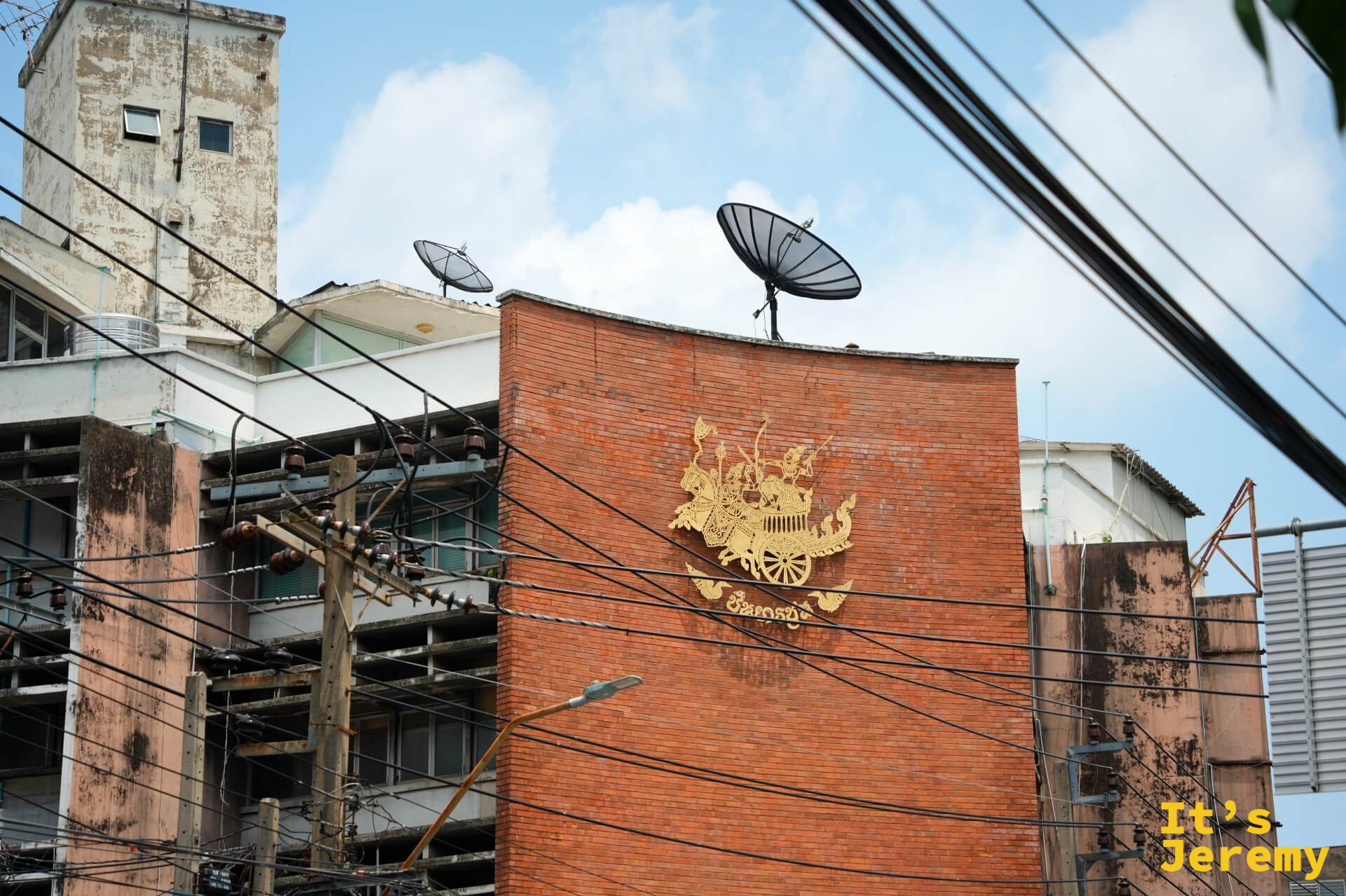 磚造老建築外牆的金色皇家徽章圖騰,背後是衛星天線和廢棄廠房