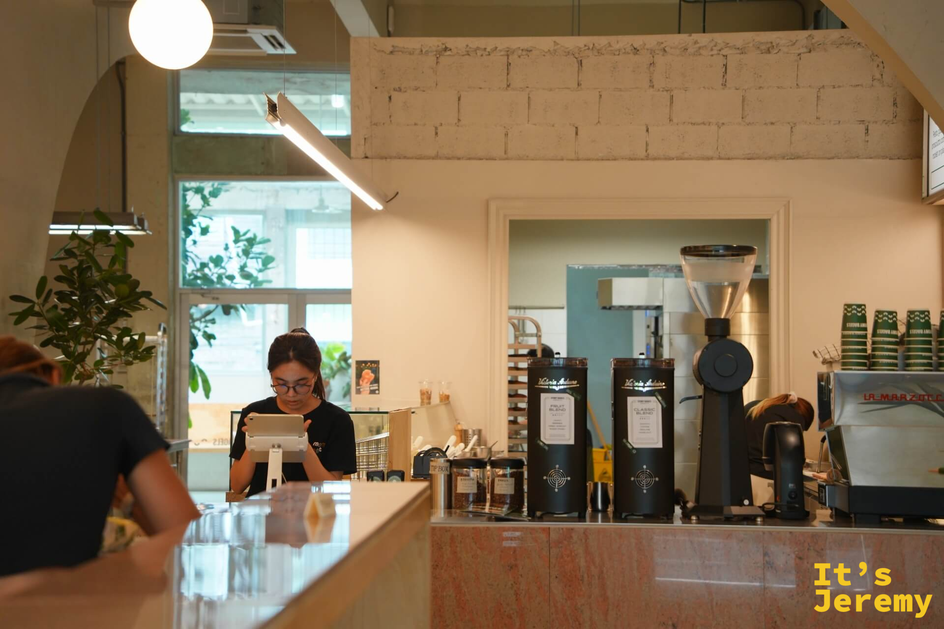 點餐台近景：La Marzocco 咖啡機、Fruit Blend 與 Classic Blend 磨豆機並排，吧台大理石台面整潔