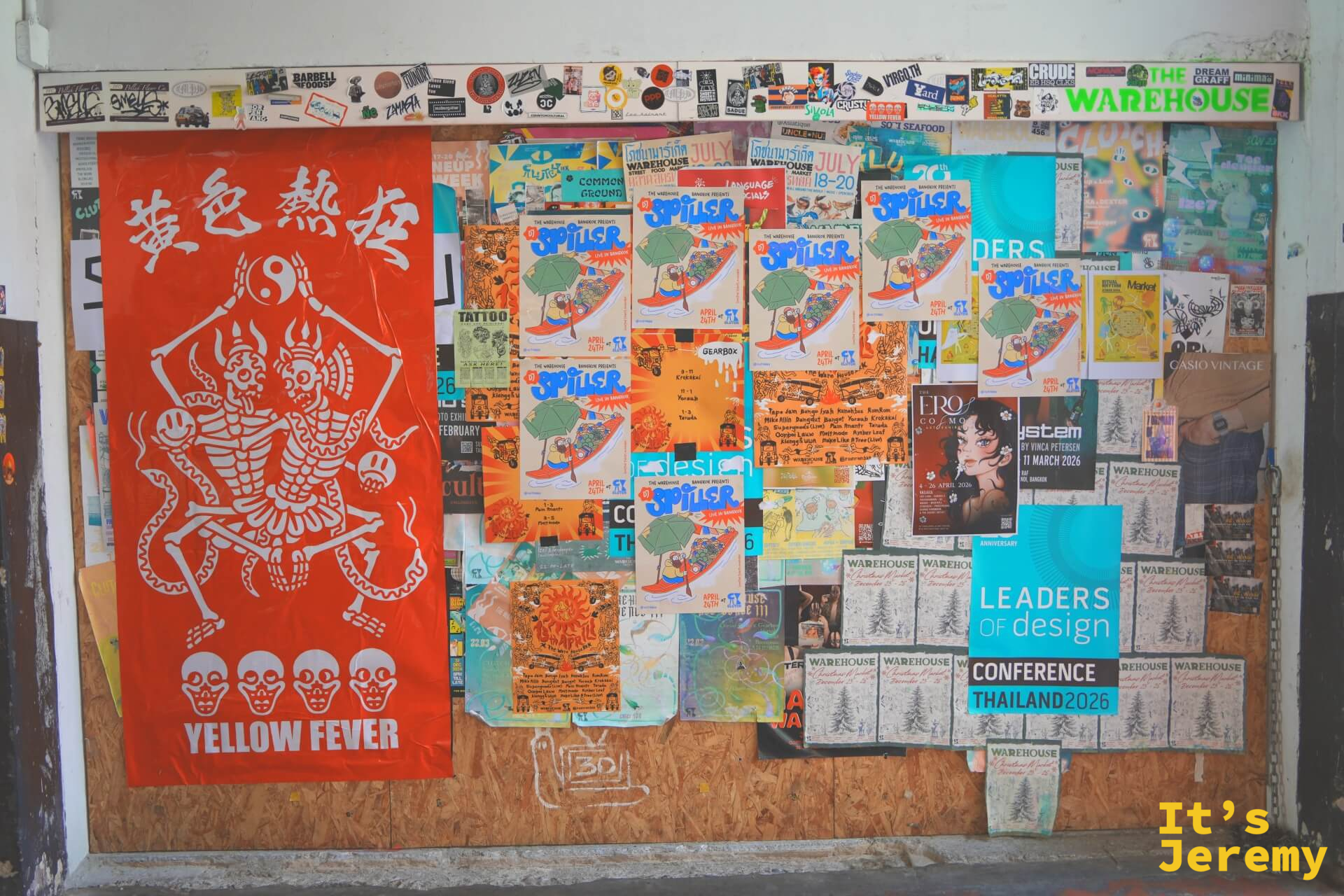公佈欄上貼著「黃色熱狂 Yellow Fever」展覽旗幟和多張活動海報,上方角落有「THE WAREHOUSE」字樣