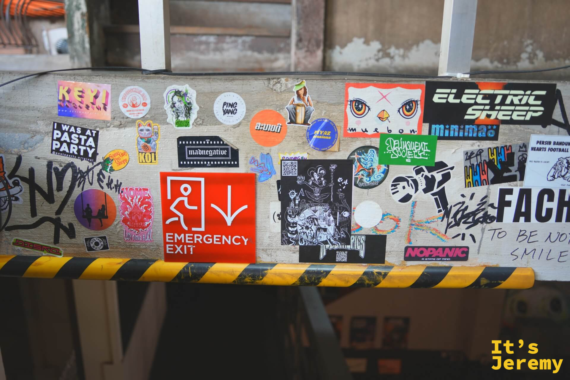 橫梁上密布貼紙:Emergency Exit 紅色標誌夾在各種品牌貼紙之間,包括 Electric Sheep、FACH 字樣