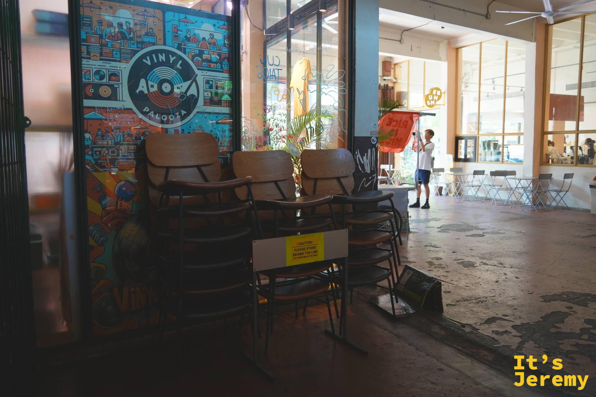 THE WAREHOUSE 一樓:Vinyl Apalooza 唱片市集的插畫海報貼在玻璃門上,前景是堆疊的木椅,空曠的水泥地
