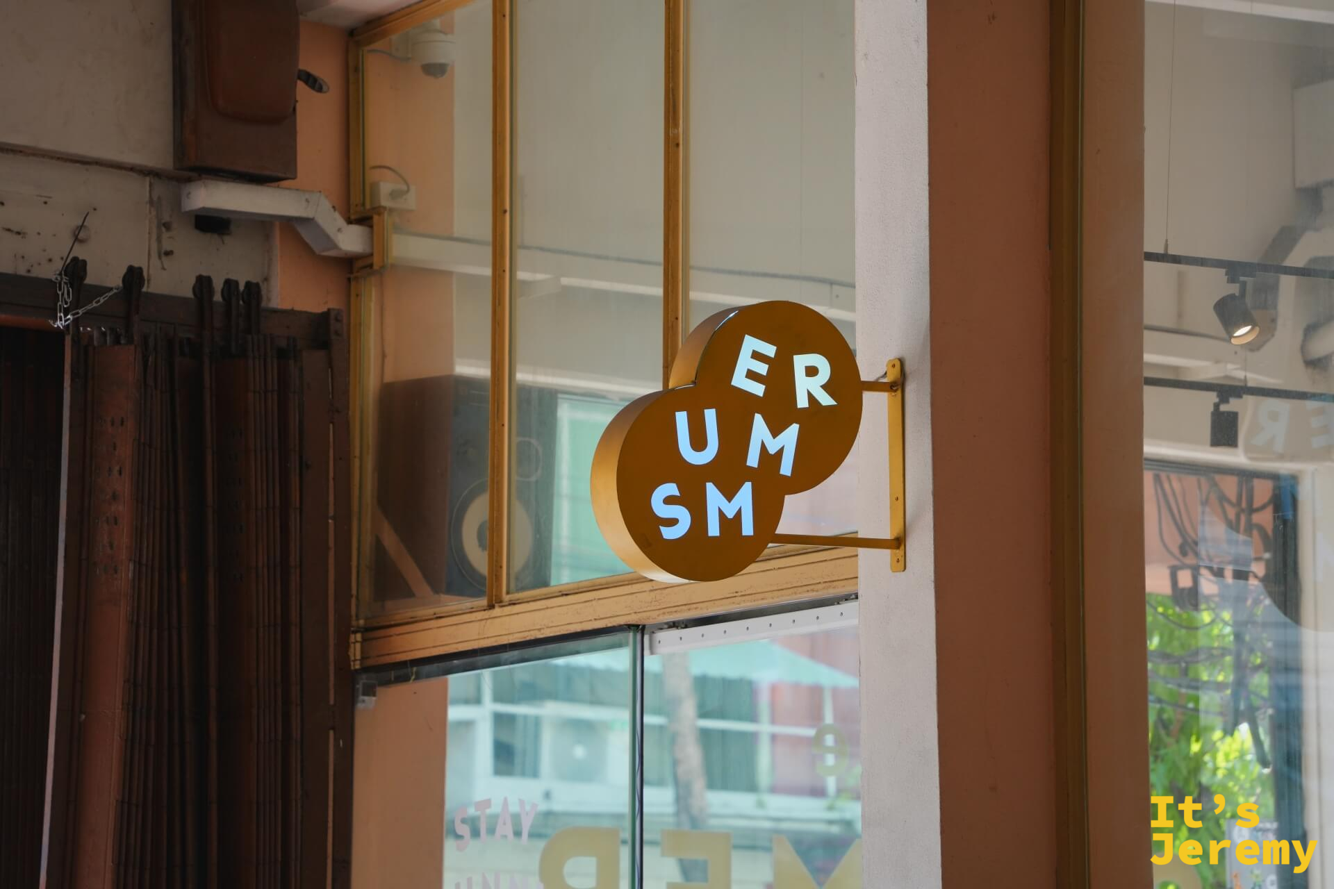 建築外側掛著咖啡色圓形招牌「ER UM SM」,後方玻璃窗內可見大型監聽音箱