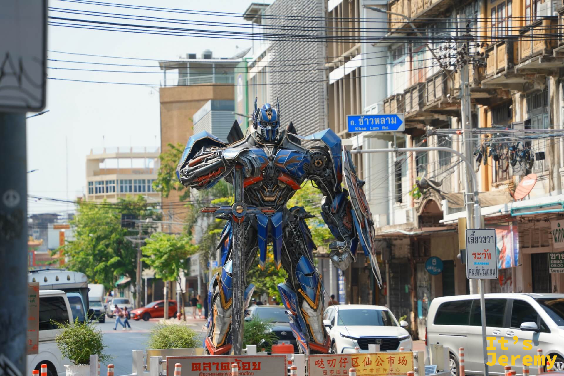 路口矗立的藍銀色金屬廢料拼組擎天柱雕塑,背後是街道和天空