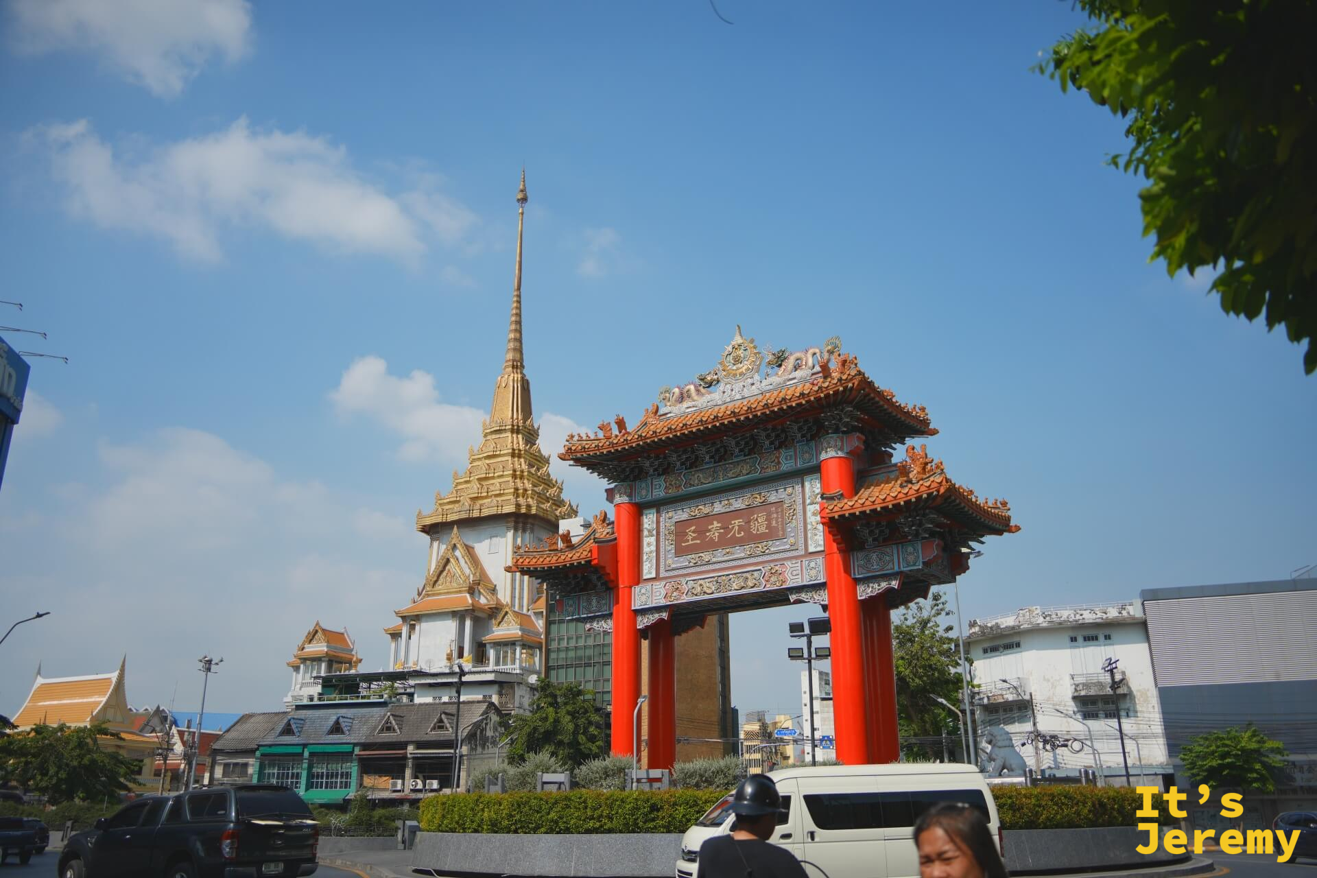 大型中式彩繪牌樓,後方可見 Wat Trimit 金佛寺的金色尖塔,藍天白雲