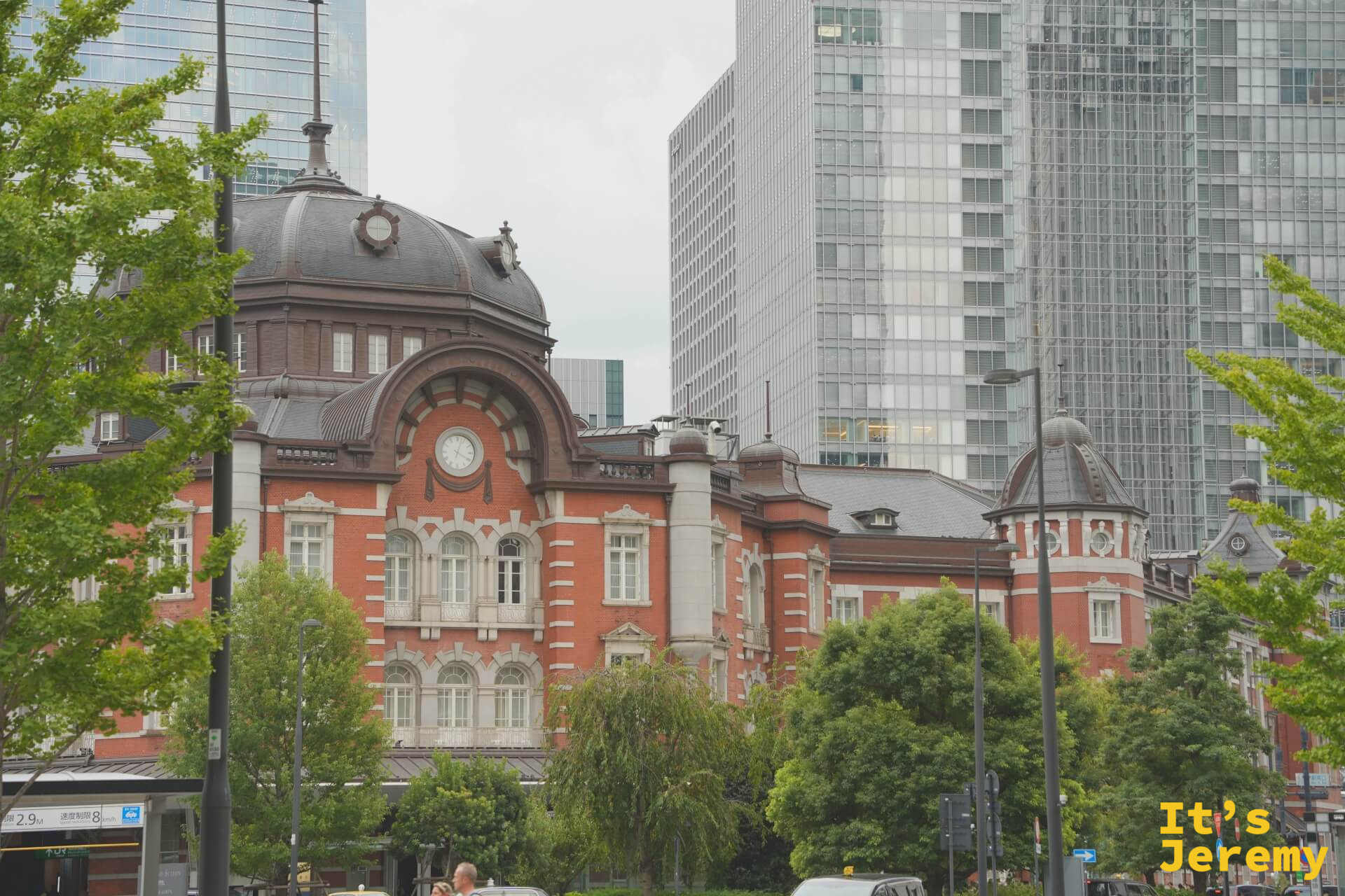 從街道旁樹叢間望向東京車站圓頂,背後是現代辦公大樓