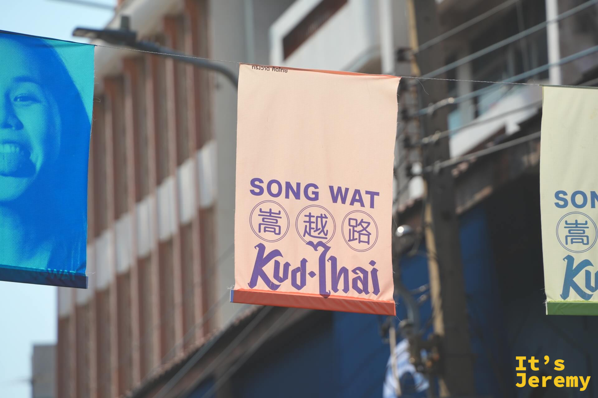 「SONG WAT 嵩越路 Kud-Thai」旗幟近景,粉橘底色搭配深色字體,嵩越路社群品牌的核心視覺