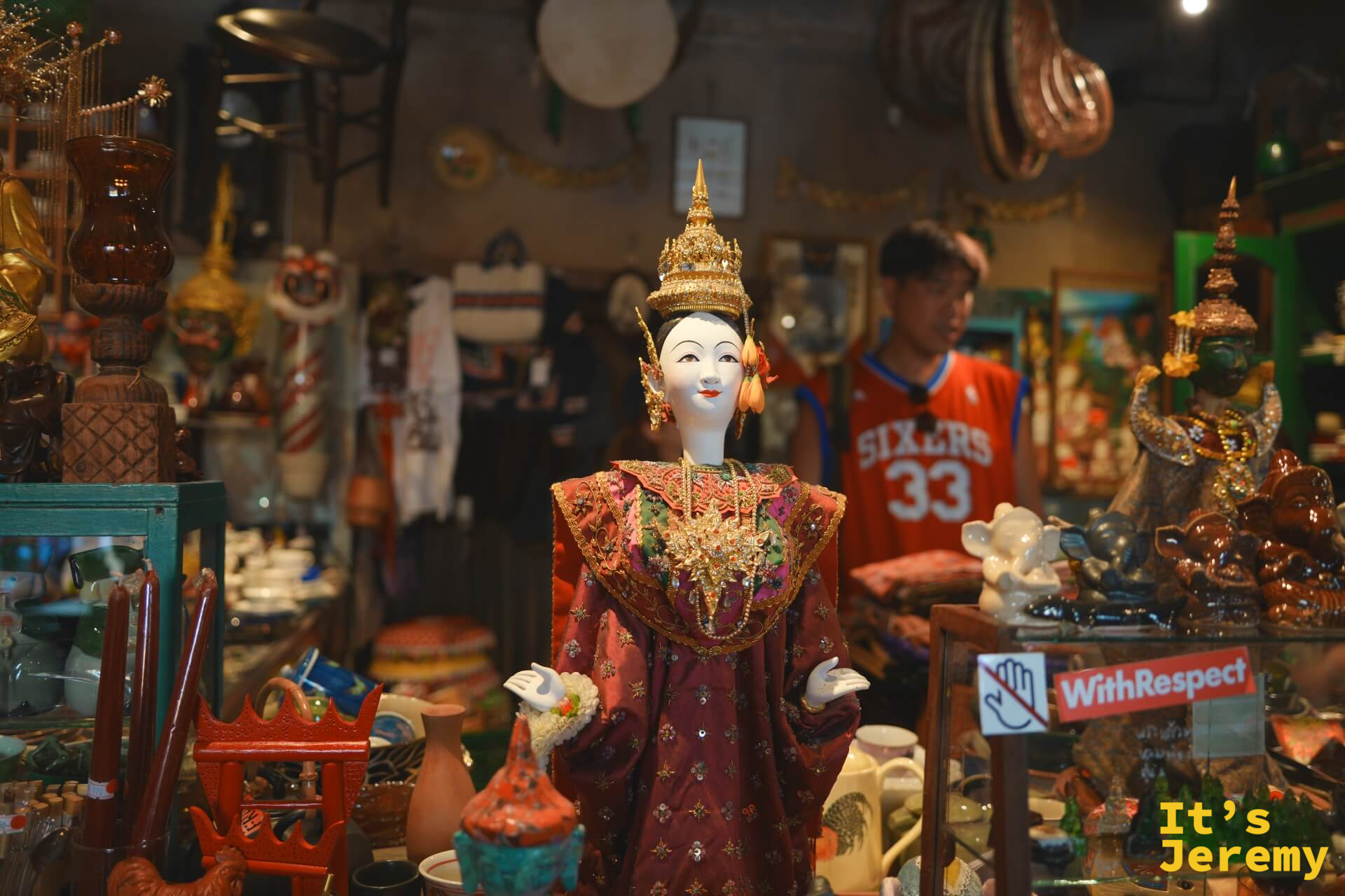 Tang Chae Studio 內的泰國古典舞者人偶,身著金冠與精工刺繡朱紅禮服,背景是古董雜物堆疊