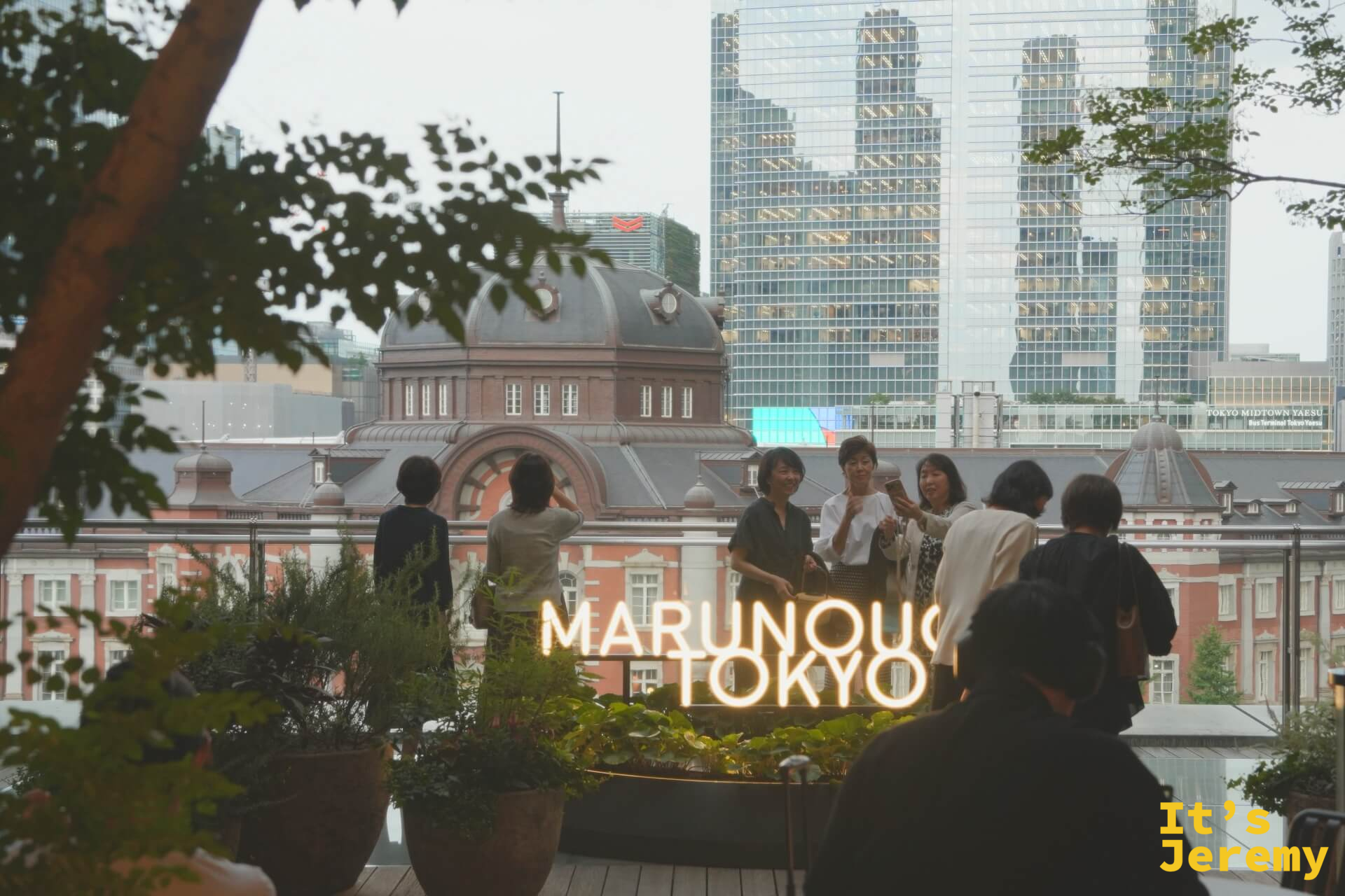MARUNOUCHI TOKYO 霓虹燈牌前,遊客聚集合影,背後是東京車站圓頂與摩天大樓