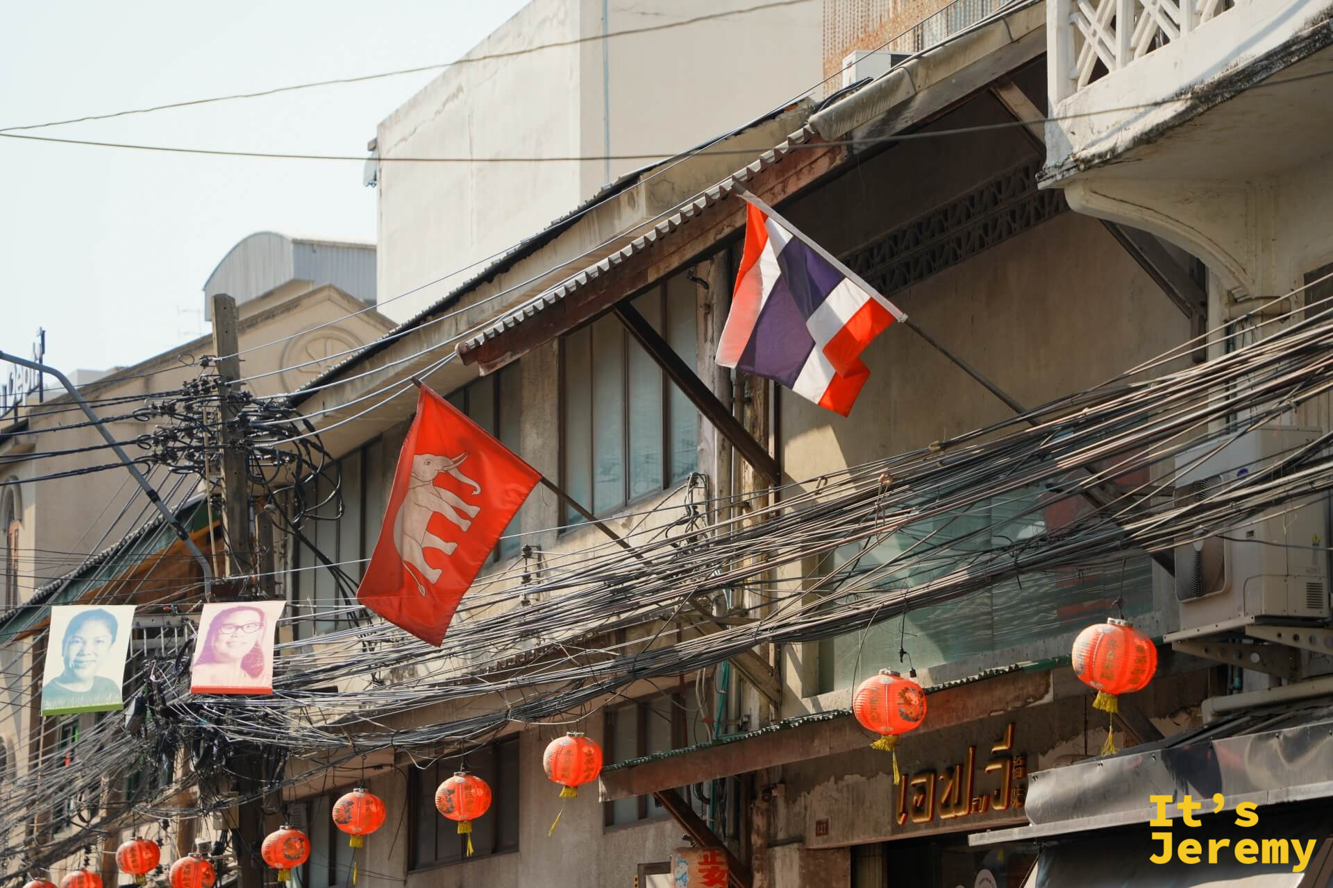 嵩越路老街屋建築一角:纏繞的電線叢、紅色布條旗幟與橘紅燈籠,百年街區的日常面貌