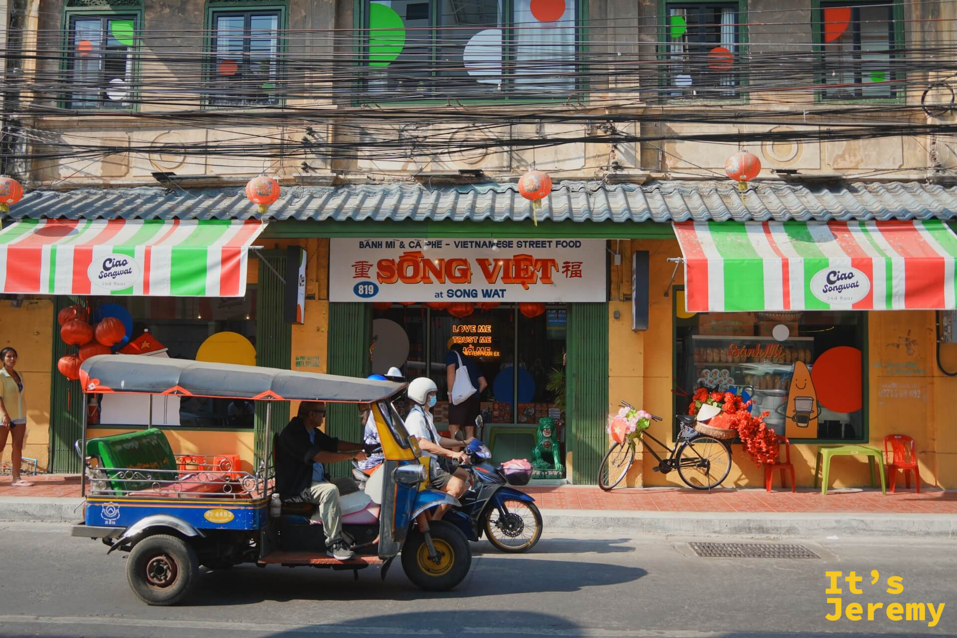 「SÔNG VIỆT 越南街頭料理」餐廳外觀,紅白條紋遮陽棚,一輛嘟嘟車從前方駛過
