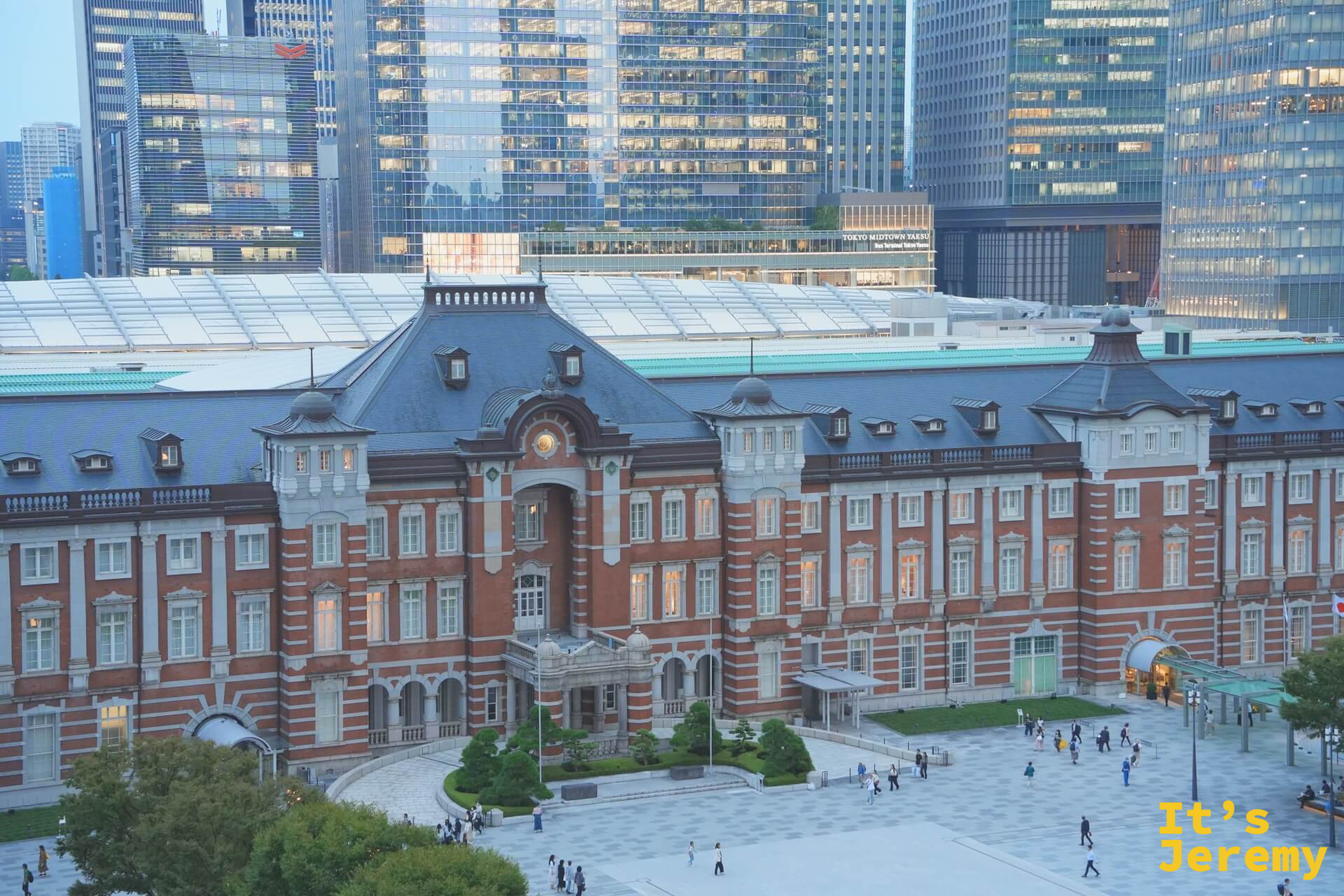 傍晚從高處俯拍丸之內廣場,東京車站站體完整展開,背後摩天大樓群隱入暮色