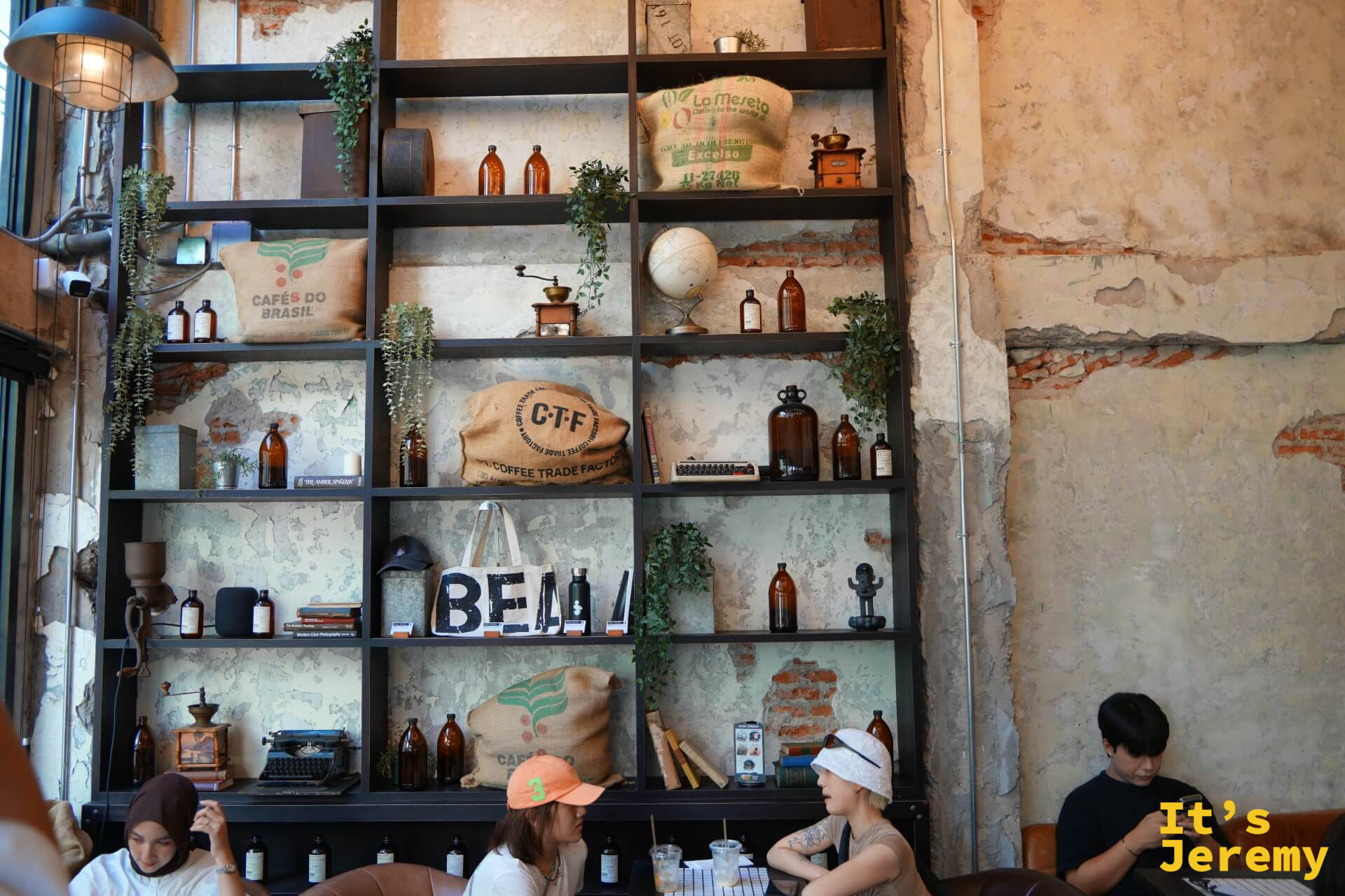 室內鐵架書牆:陳列麻布咖啡袋(Cafés do Brasil、CTF Coffee Trade Factory)、琥珀色玻璃瓶、打字機與地球儀,斑駁石灰牆面作為背景