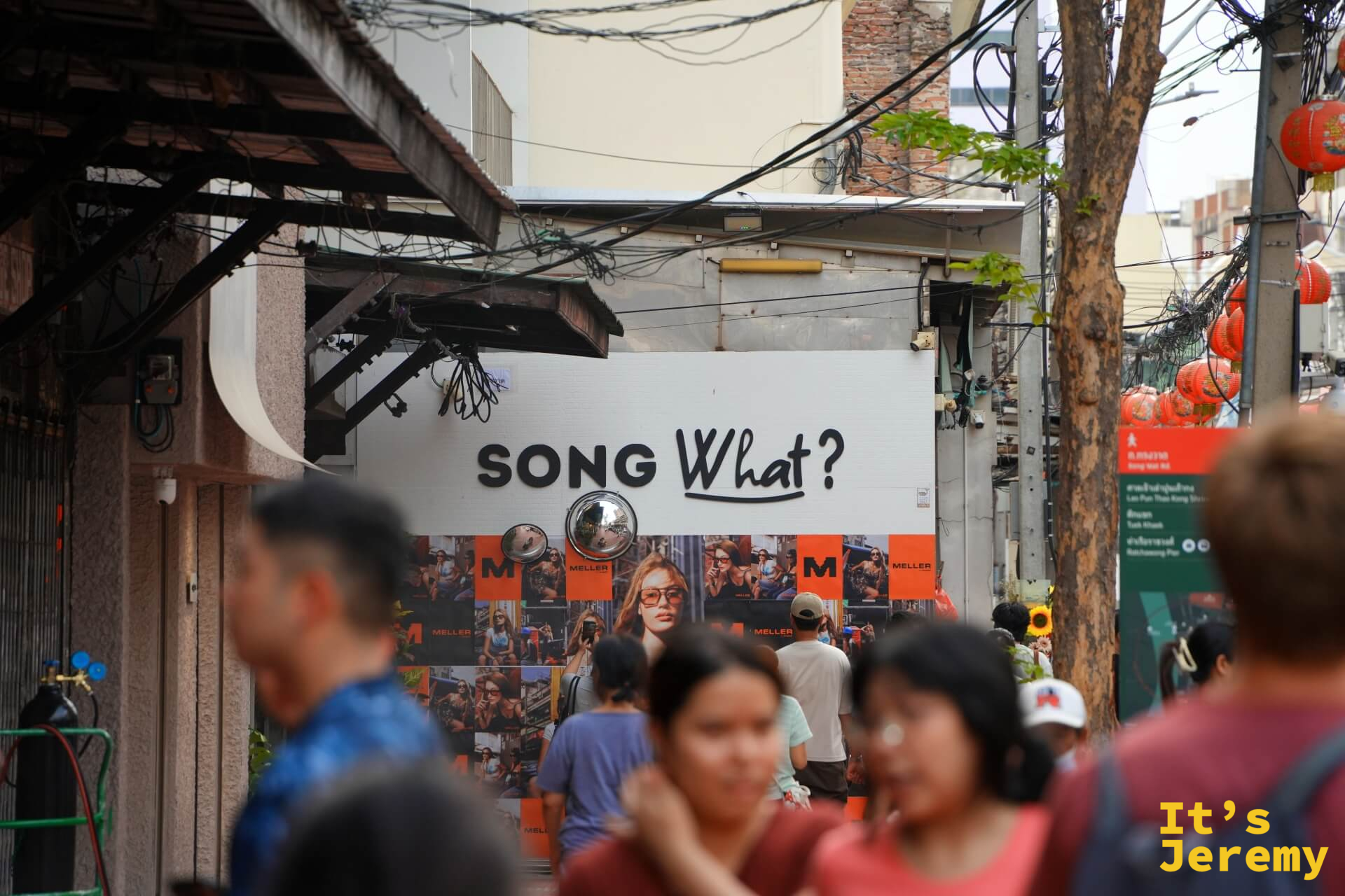 「SONG What?」大字貼在巷口建築外牆,前景是人群,背後有紅燈籠和嵩越路路標