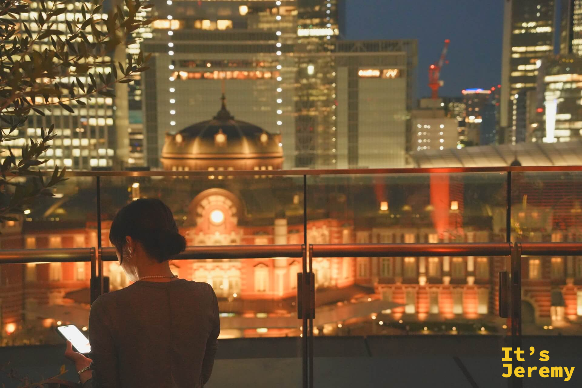 露台女性背影,東京車站橘紅夜景在玻璃護欄上透出倒影