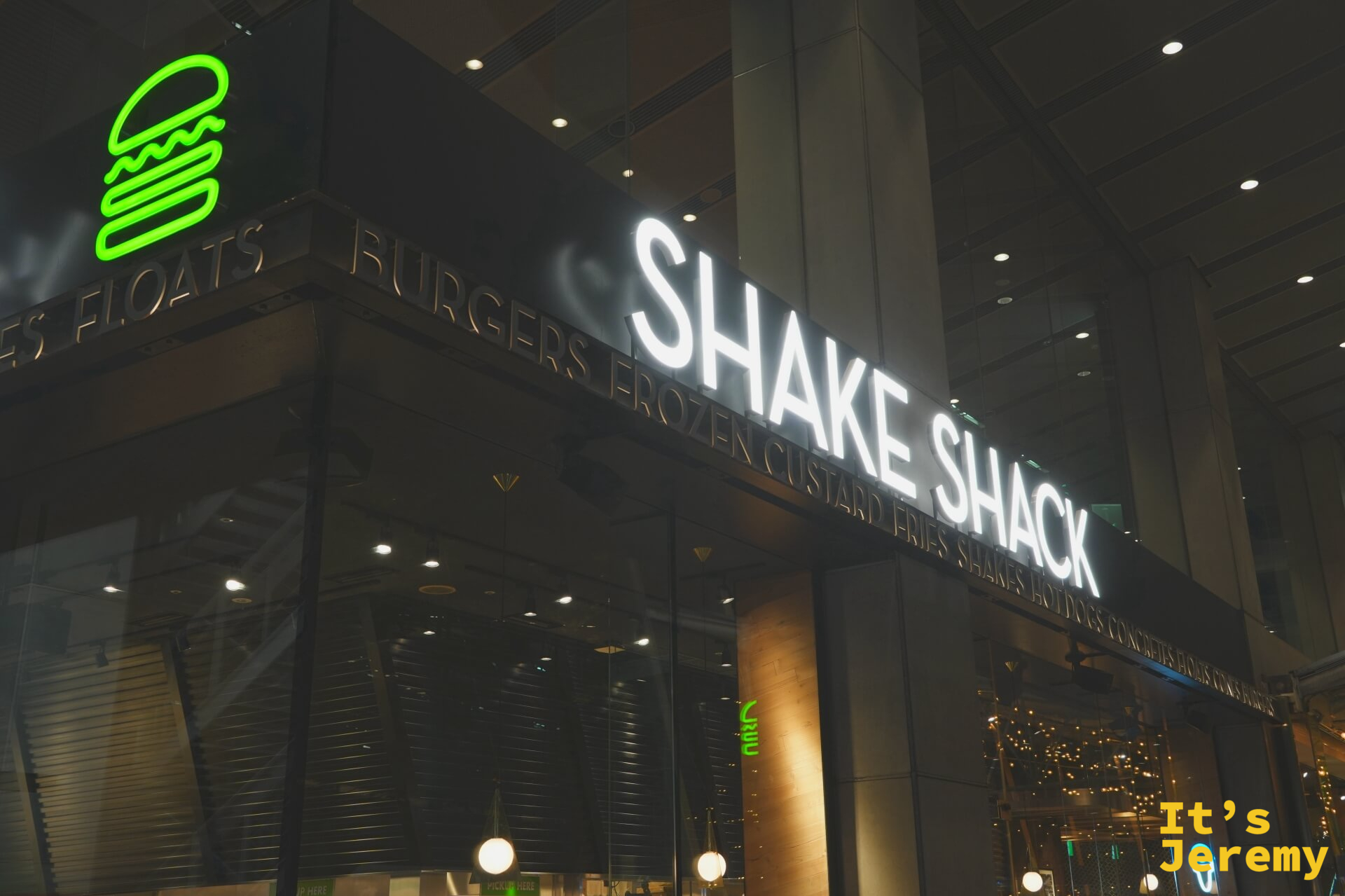 Shake Shack 東京國際論壇店店面招牌，白色燈箱大字與綠色霓虹漢堡 logo，夜間拍攝