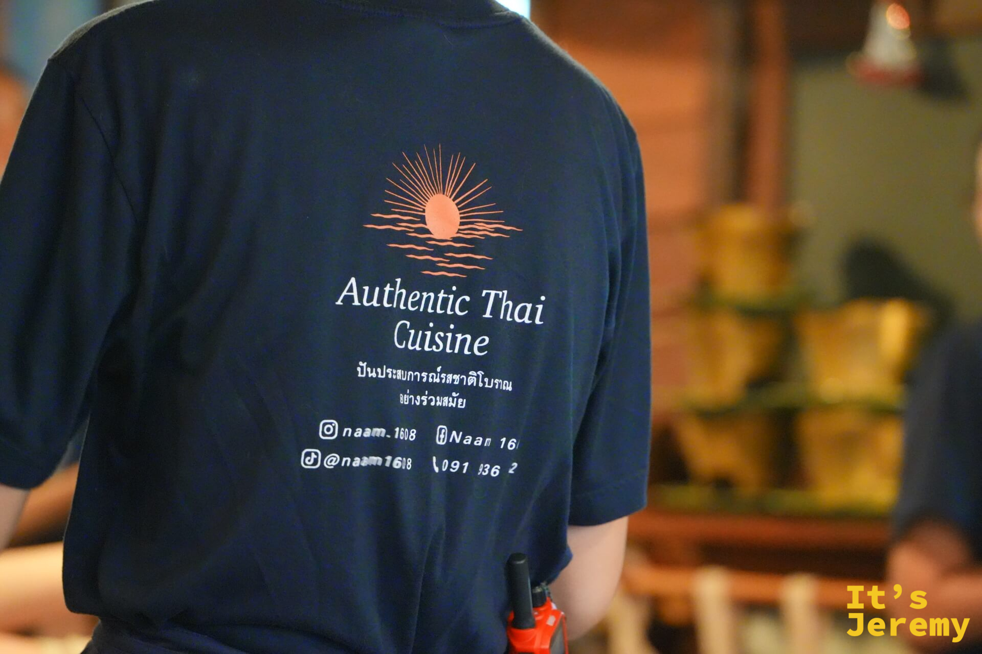 服務員背影，T-shirt 後背清楚印著「Authentic Thai Cuisine」字樣