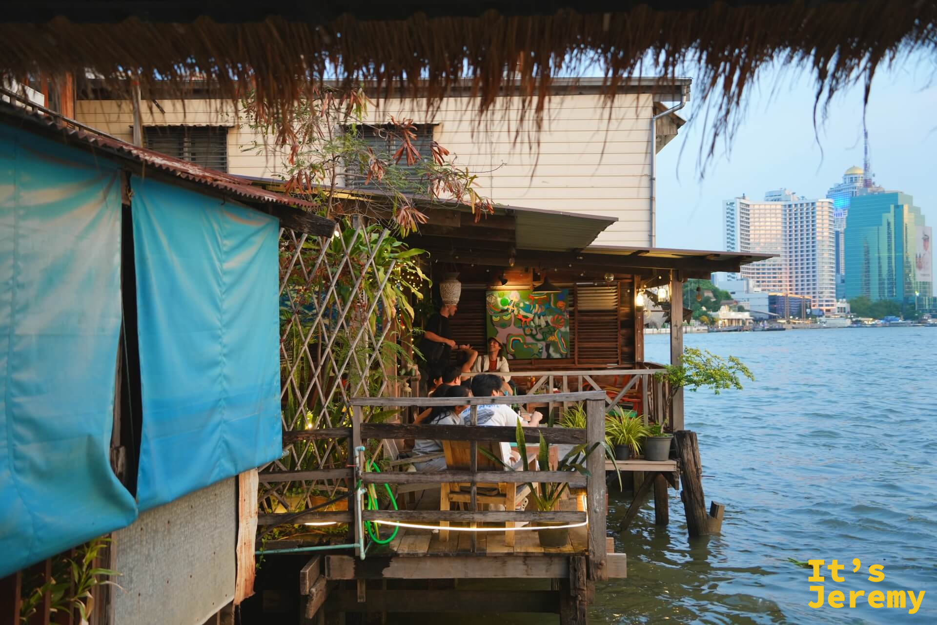 NAAM 1608 餐廳外觀，木製老屋結構緊靠昭披耶河，對岸可見曼谷市區高樓輪廓