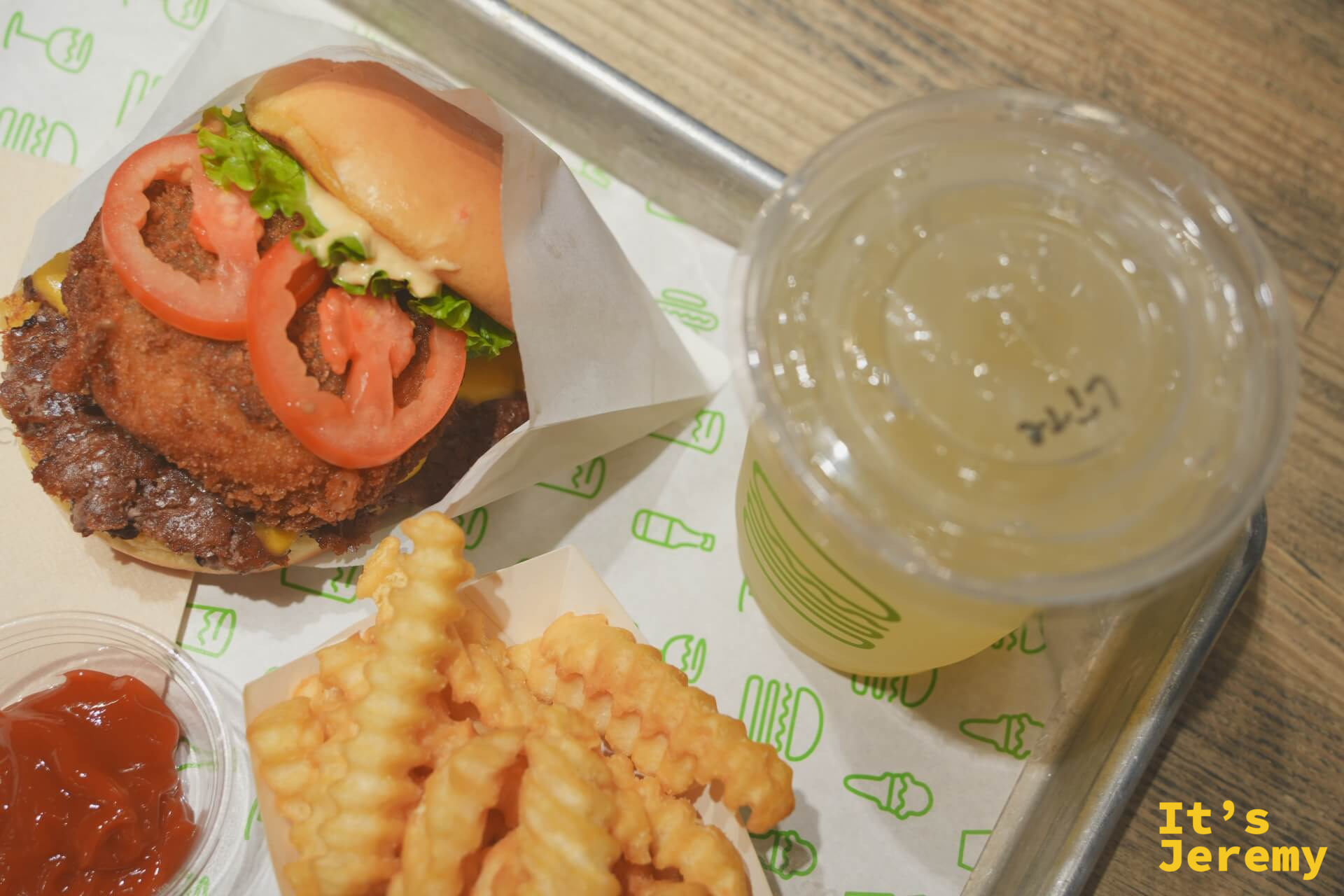 俯瞰角度的 ShackStack、波浪薯條與檸檬水，托盤鋪有 Shake Shack 品牌圖案紙