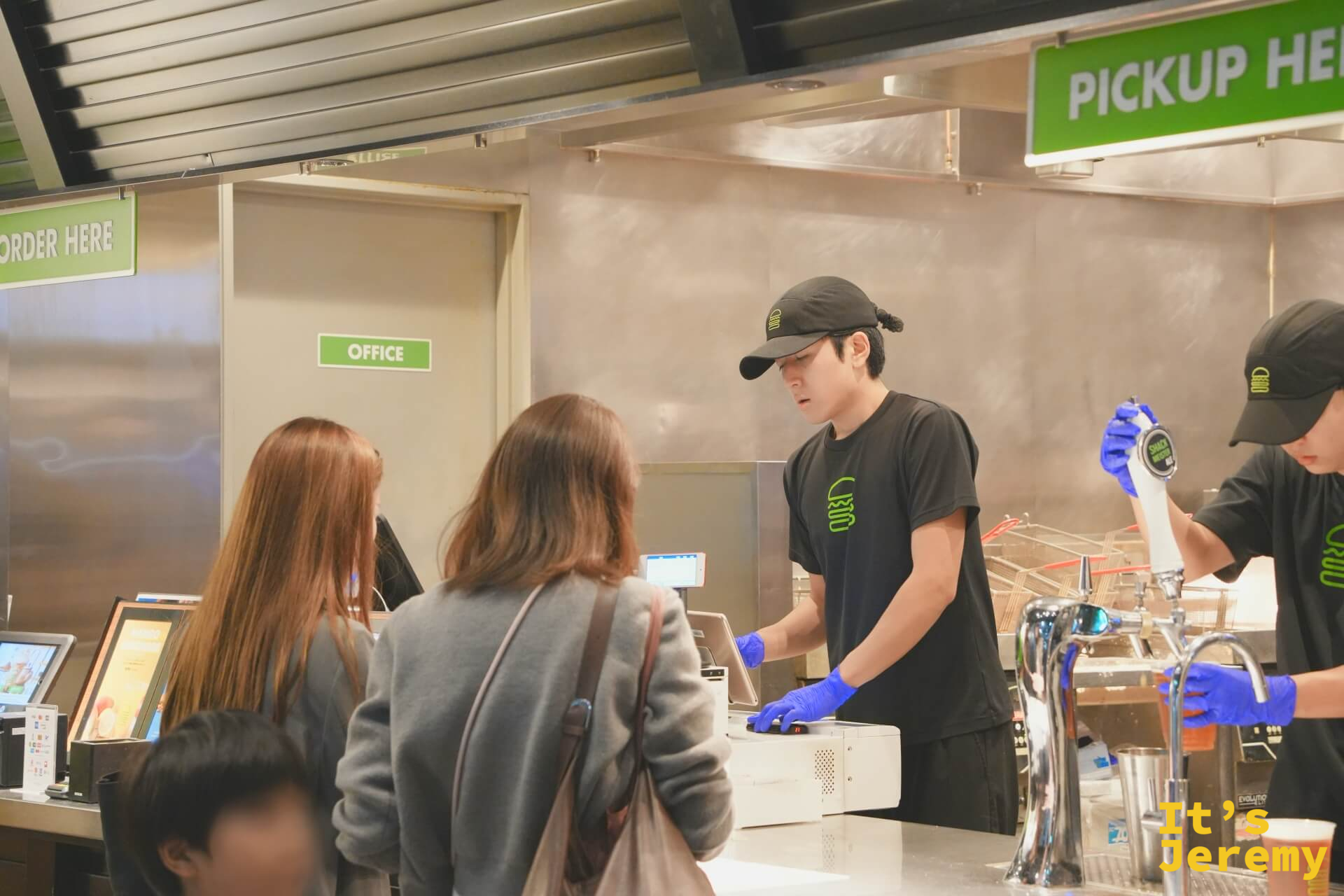 點餐台，顧客在人工櫃台前排隊，店員正在確認訂單，後方生啤機區域同時在出餐