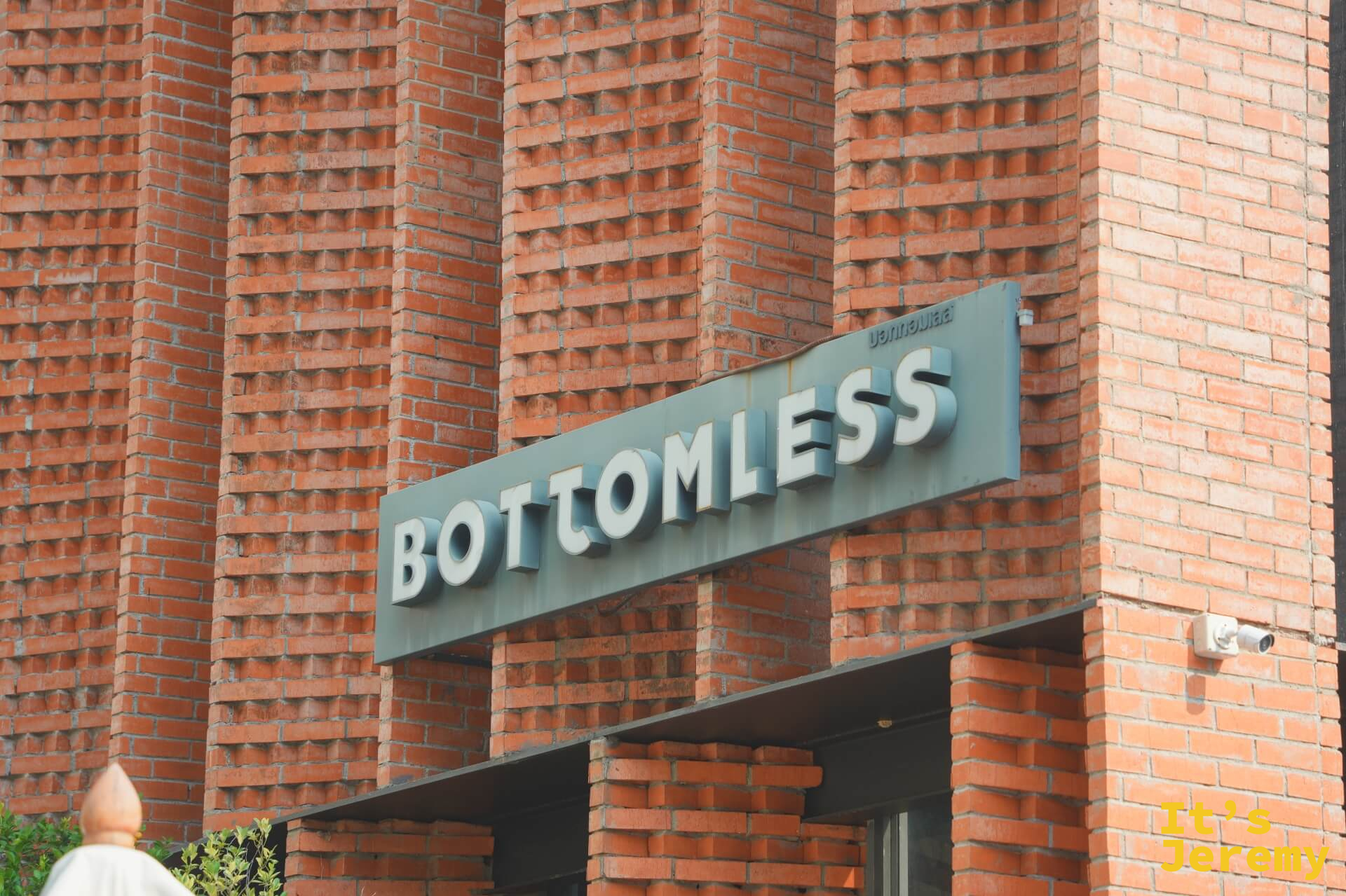 建築主入口旁的 BOTTOMLESS 金屬字招牌，鑲嵌在紅磚牆上