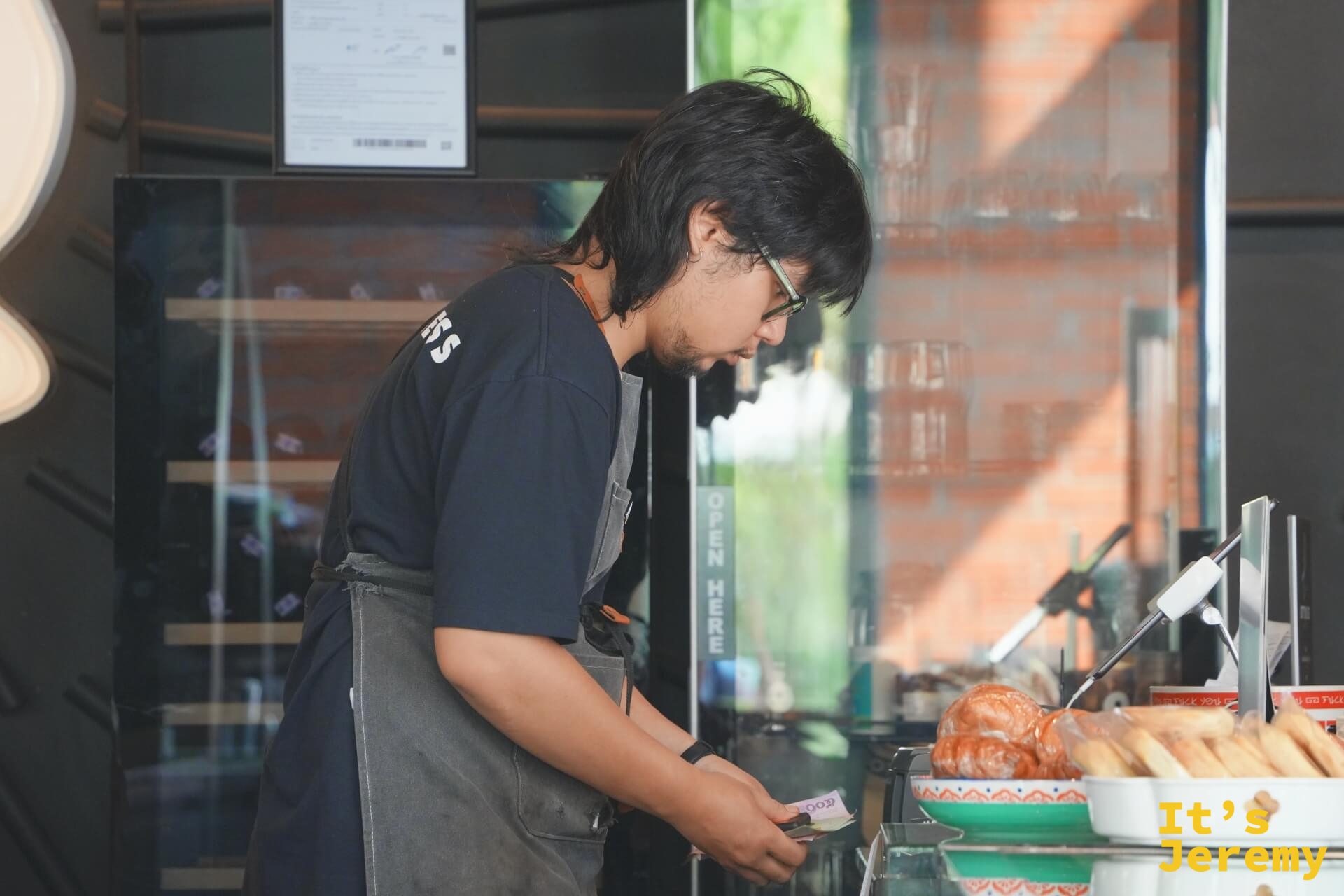 BOTTOMLESS 男性咖啡師在一樓吧台前工作，側面鏡頭，旁邊有展示甜點