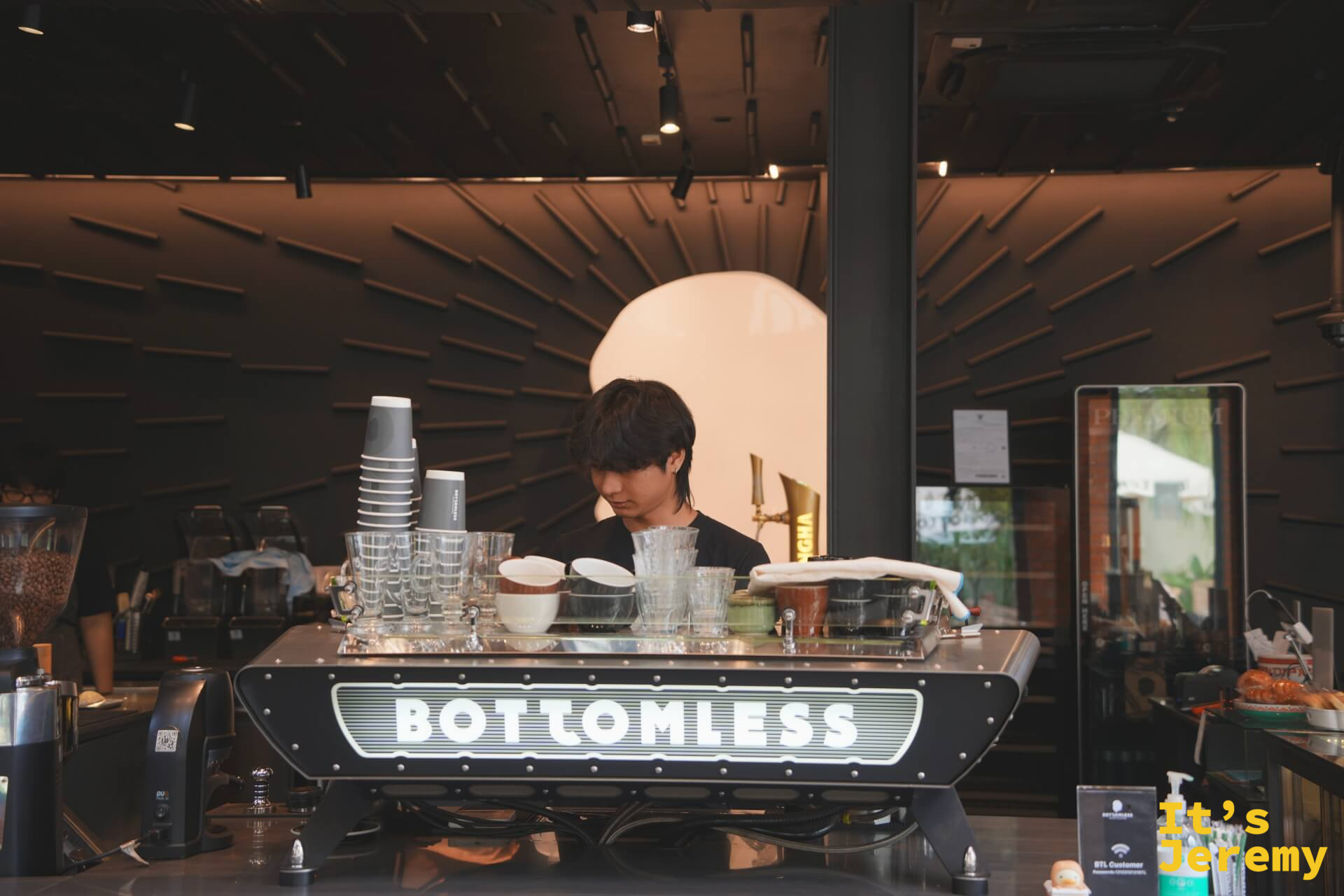 BOTTOMLESS 一樓主咖啡機，機身印有白色霓虹招牌字，背後有咖啡師在工作