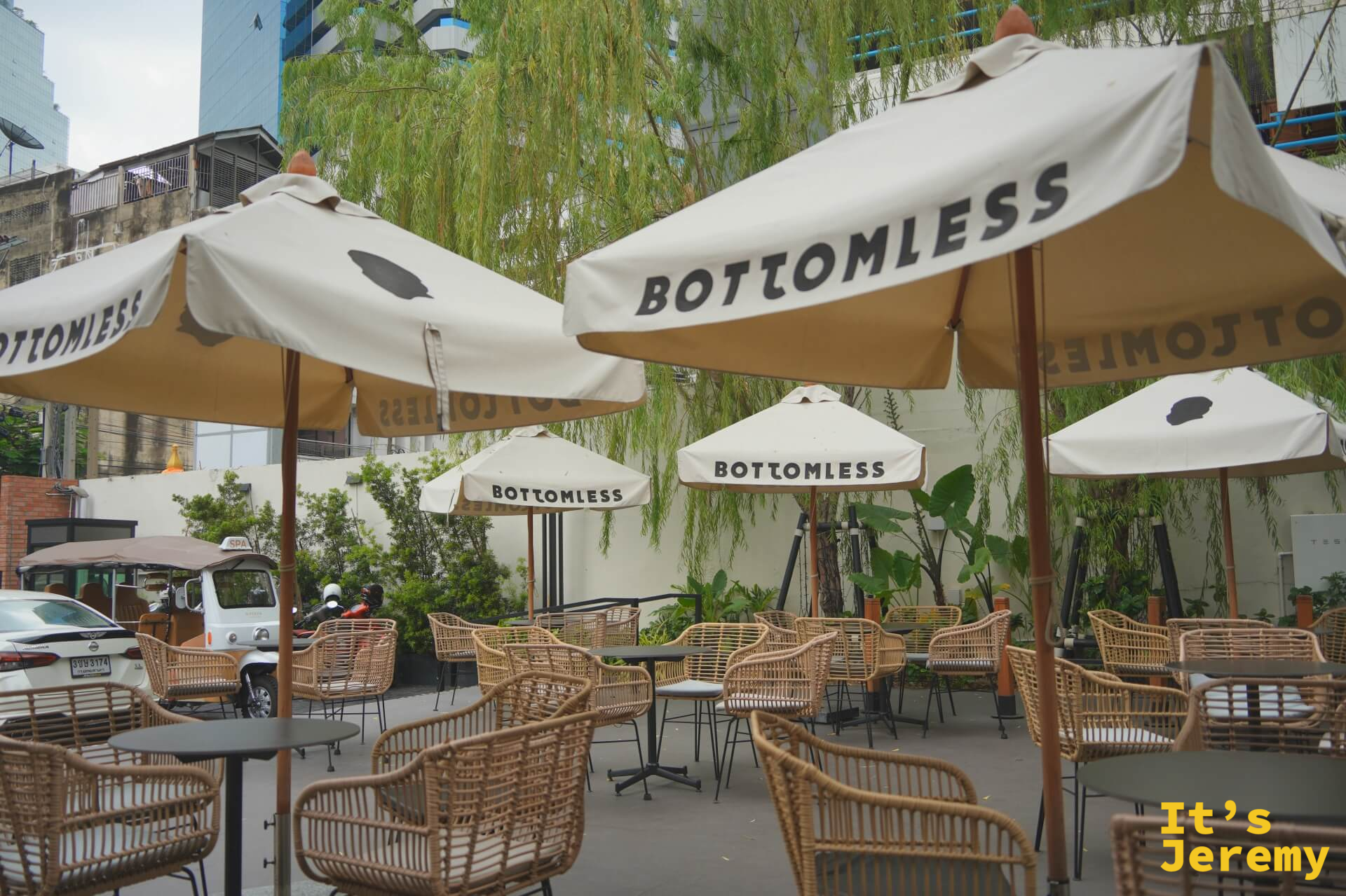 戶外庭院另一角度，多把 BOTTOMLESS 品牌傘排列，背後可見曼谷街景