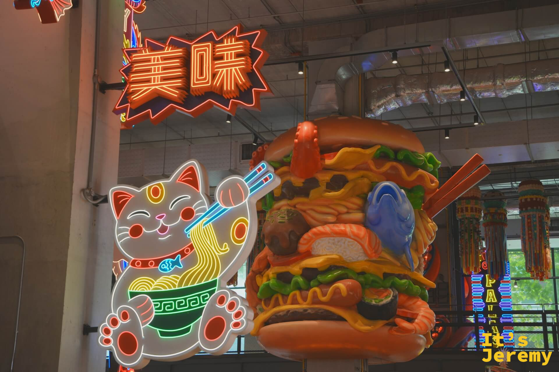 招財貓吃拉麵的霓虹燈牌與「美味」霓虹字樣,右邊是巨型食物混搭雕塑