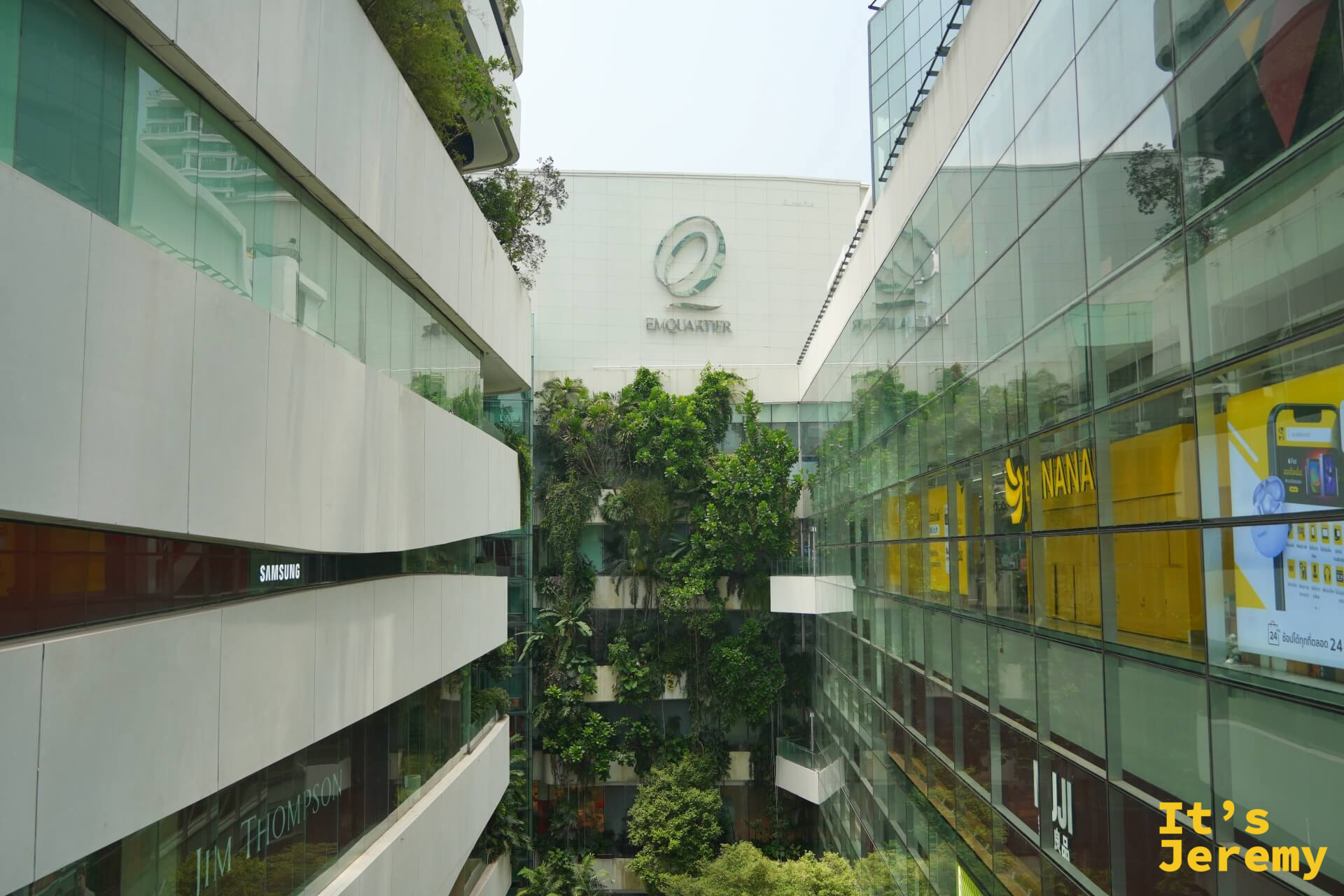 EmQuartier 中庭俯視,兩棟玻璃建築夾著綠意中庭,可見 EmQuartier logo、Jim Thompson 等品牌招牌