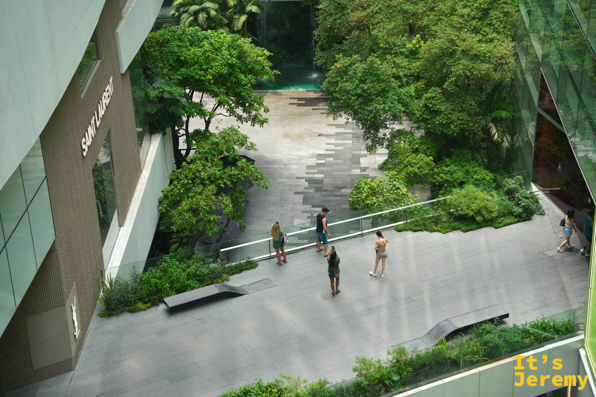 EmQuartier 戶外花園廣場,石板地面,有旅客在樹下走動或站立