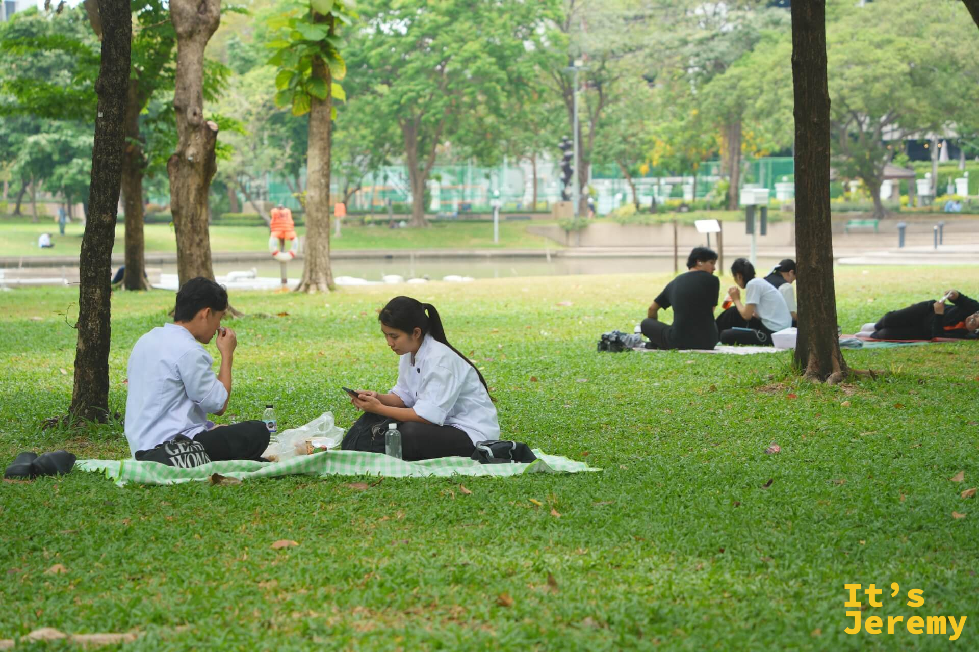 兩名穿制服的學生坐在班哲希利公園草地上,其中一人滑手機