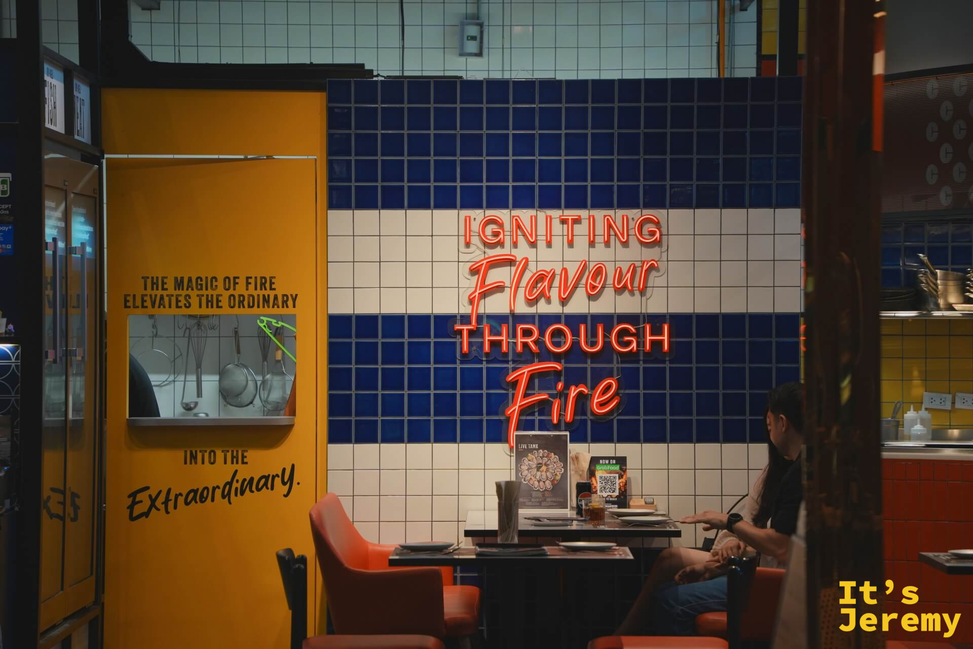 餐廳入口,藍白磁磚牆上霓虹「Igniting Flavour Through Fire」字樣,橙色椅子,食客就座