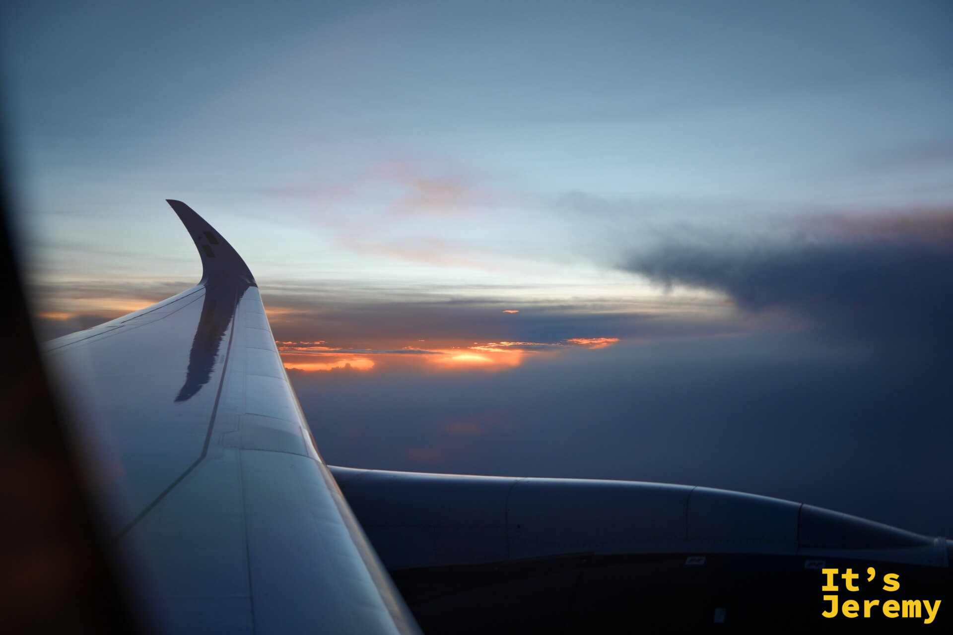 星宇航空飛機機翼與傍晚雲層,橘紅色日落光線穿透雲間,天空漸層從橘至藍