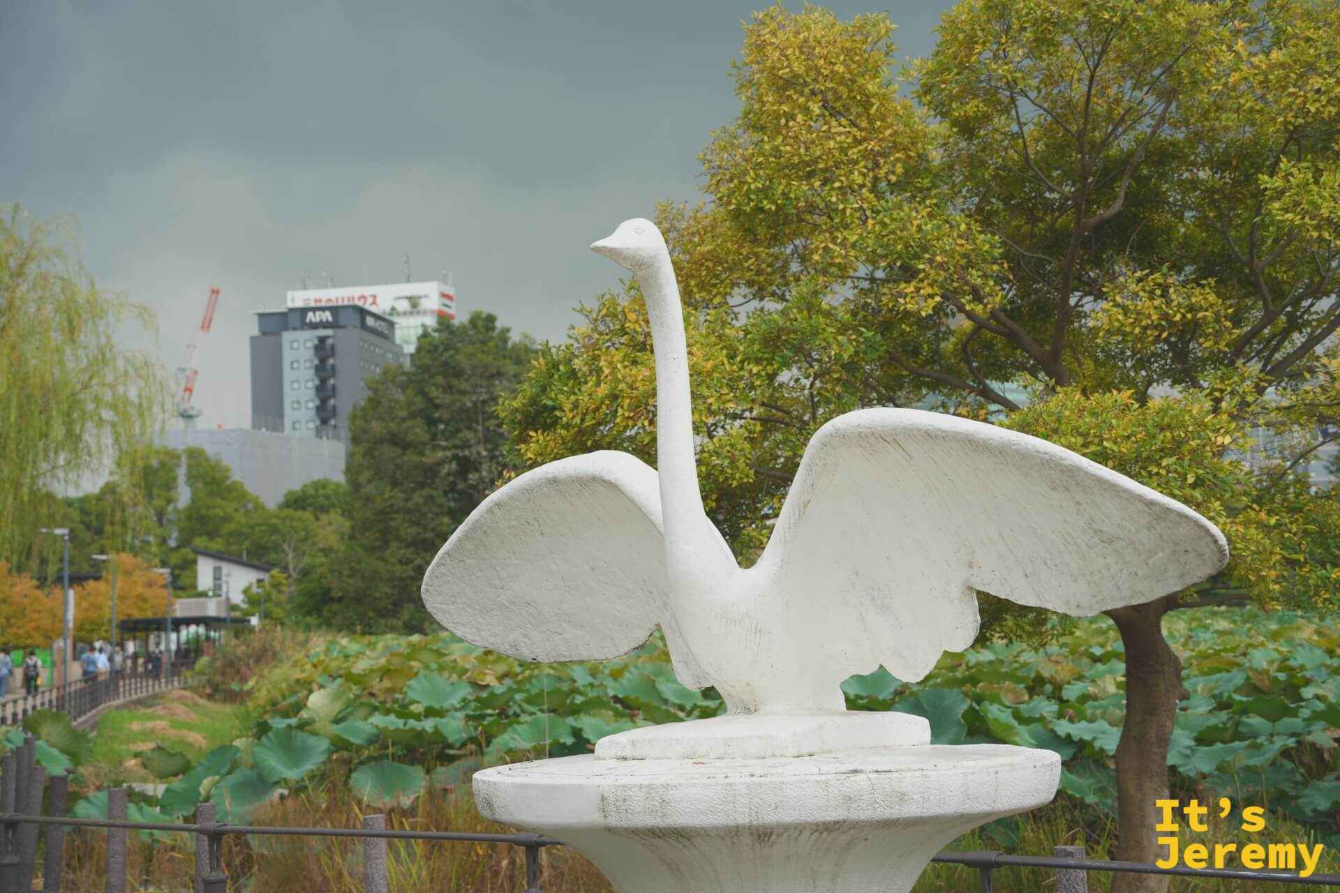 不忍池旁的白色天鵝展翅雕塑,背後是厚重的雲層和城市建築