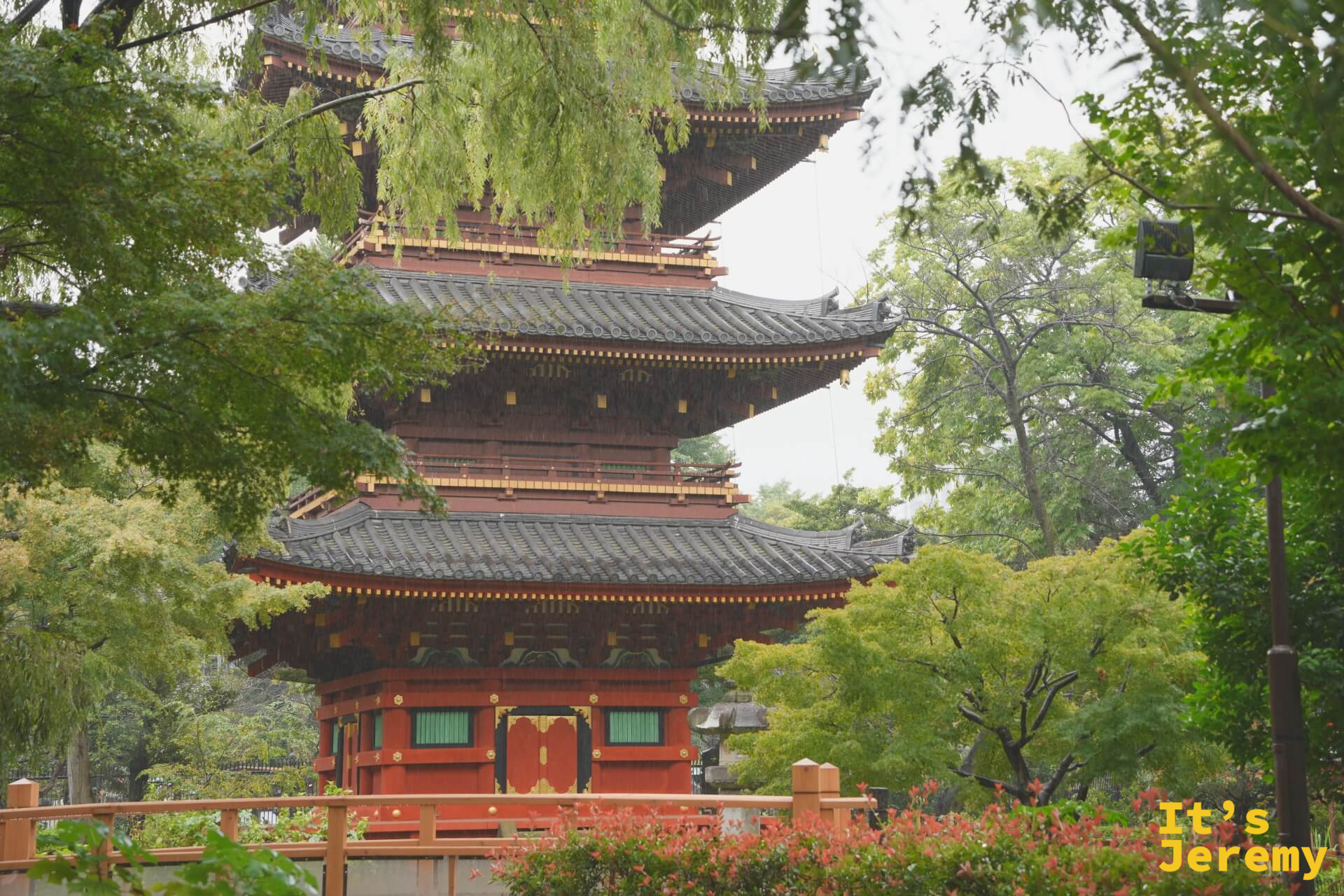 五重塔正面遠景,紅色塔身在翠綠樹木中很有分量,塔前有小橋和花叢