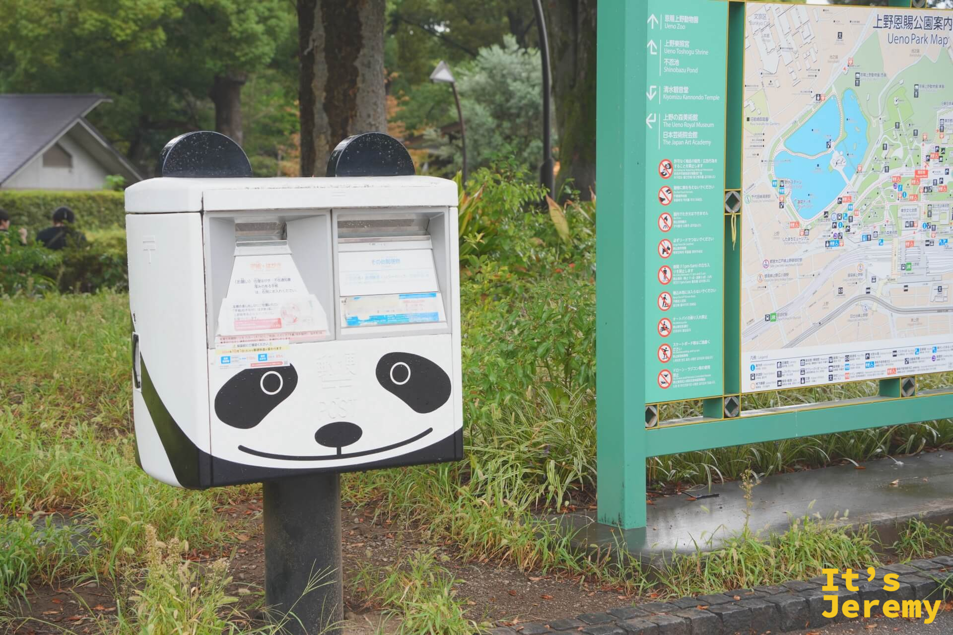 上野公園入口旁的熊貓造型收集箱，白色機體配上黑色眼鼻，旁邊是上野公園的區域地圖指示牌