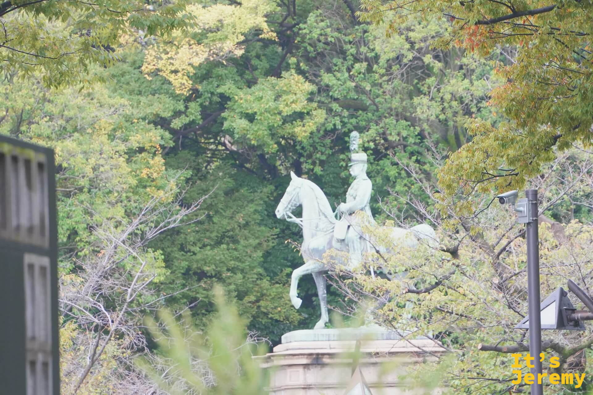 上野公園附近的騎馬銅像，青銅色的人馬雕塑在翠綠樹木的環繞之中，背景天空帶著淡淡的霧氣