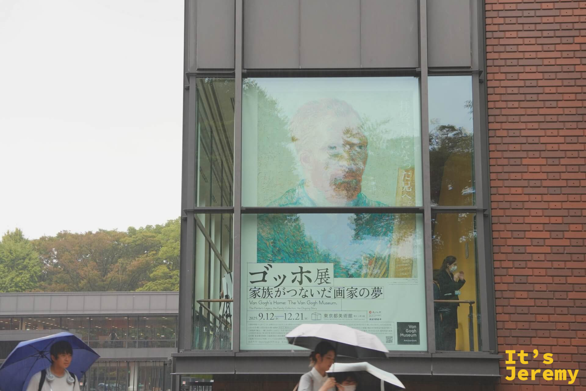 東京都美術館建築的大型玻璃外牆，映著梵谷展「ゴッホ展 家族がつないだ画家の夢」的宣傳海報，梵谷的臉透過玻璃反光以一種奇特的方式浮現在磚牆和樹影之間