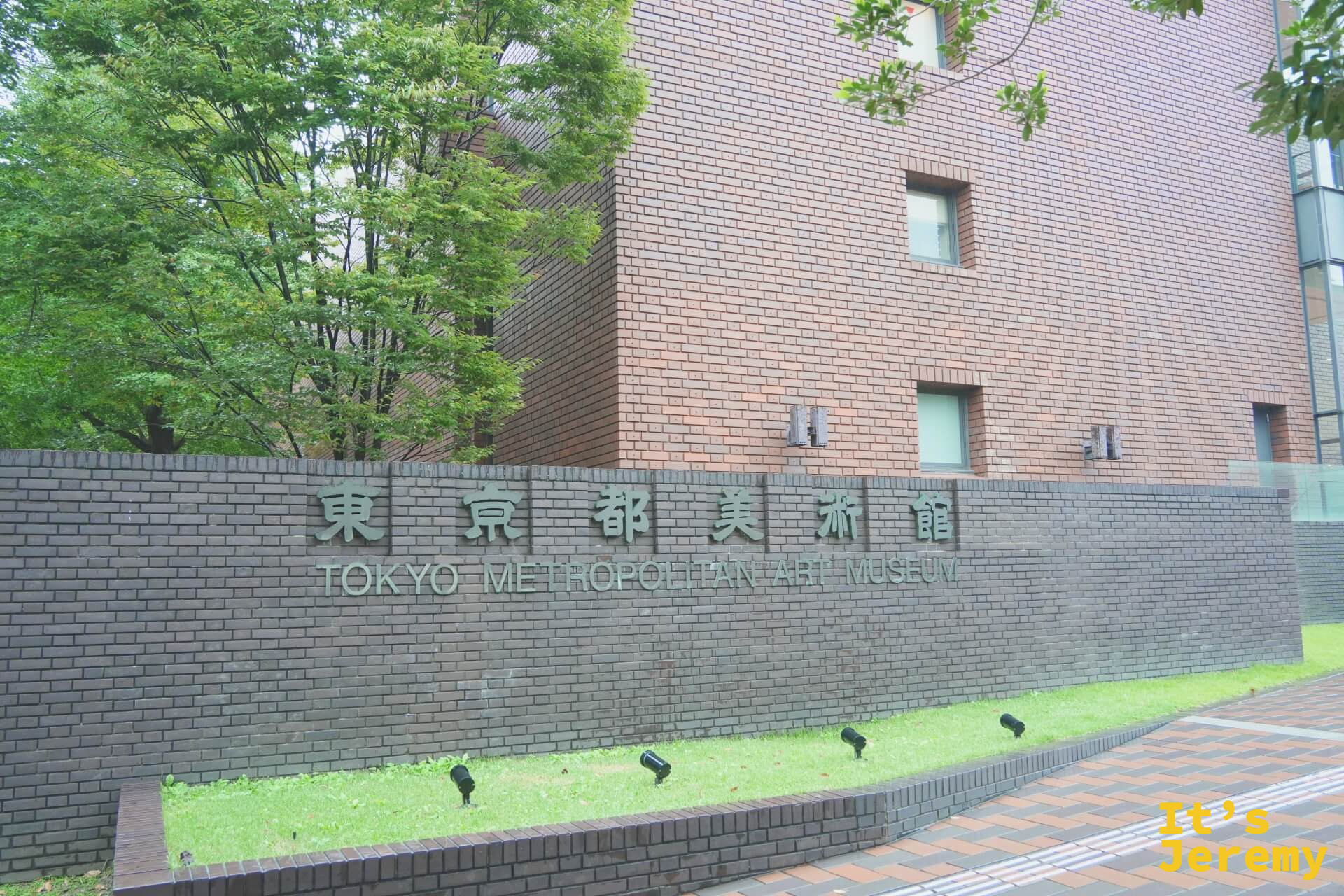 東京都美術館外牆的「東京都美術館 TOKYO METROPOLITAN ART MUSEUM」字樣牌匾，磚紅色外牆配上深綠色植栽