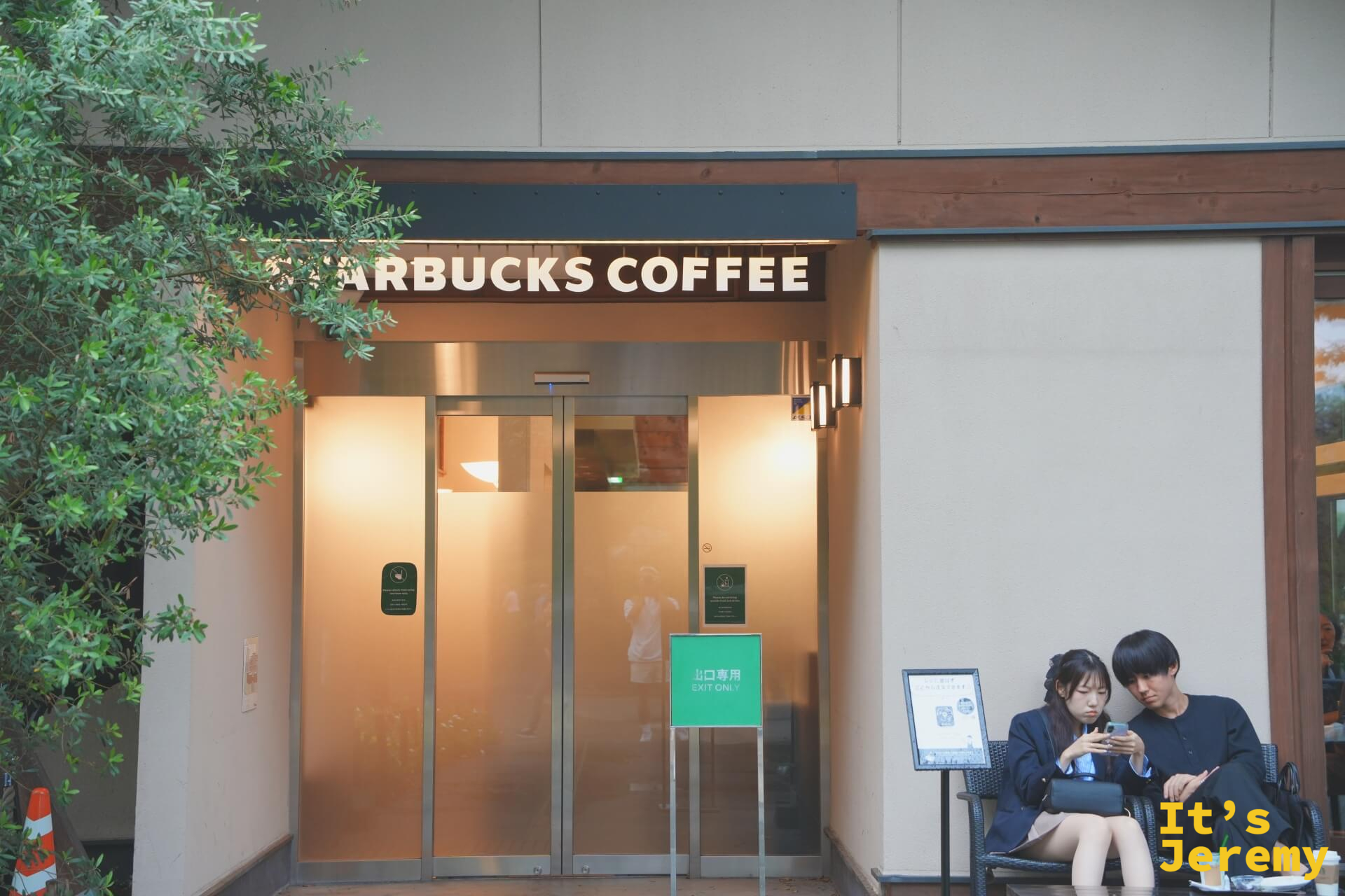 星巴克上野公園店外觀近景，玻璃門旁的「EXIT ONLY」出口牌，一對情侶並肩坐在戶外椅上各自看著手機