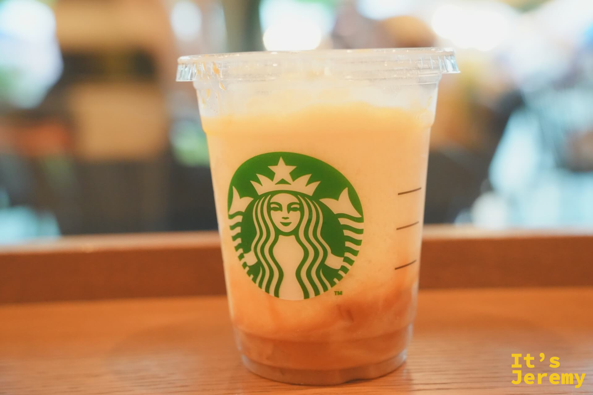 星巴克洋なし生キャラメルフラペチーノ，橘黃色奶泡的飲料放在木桌上，星巴克綠色女神 logo 清晰可見