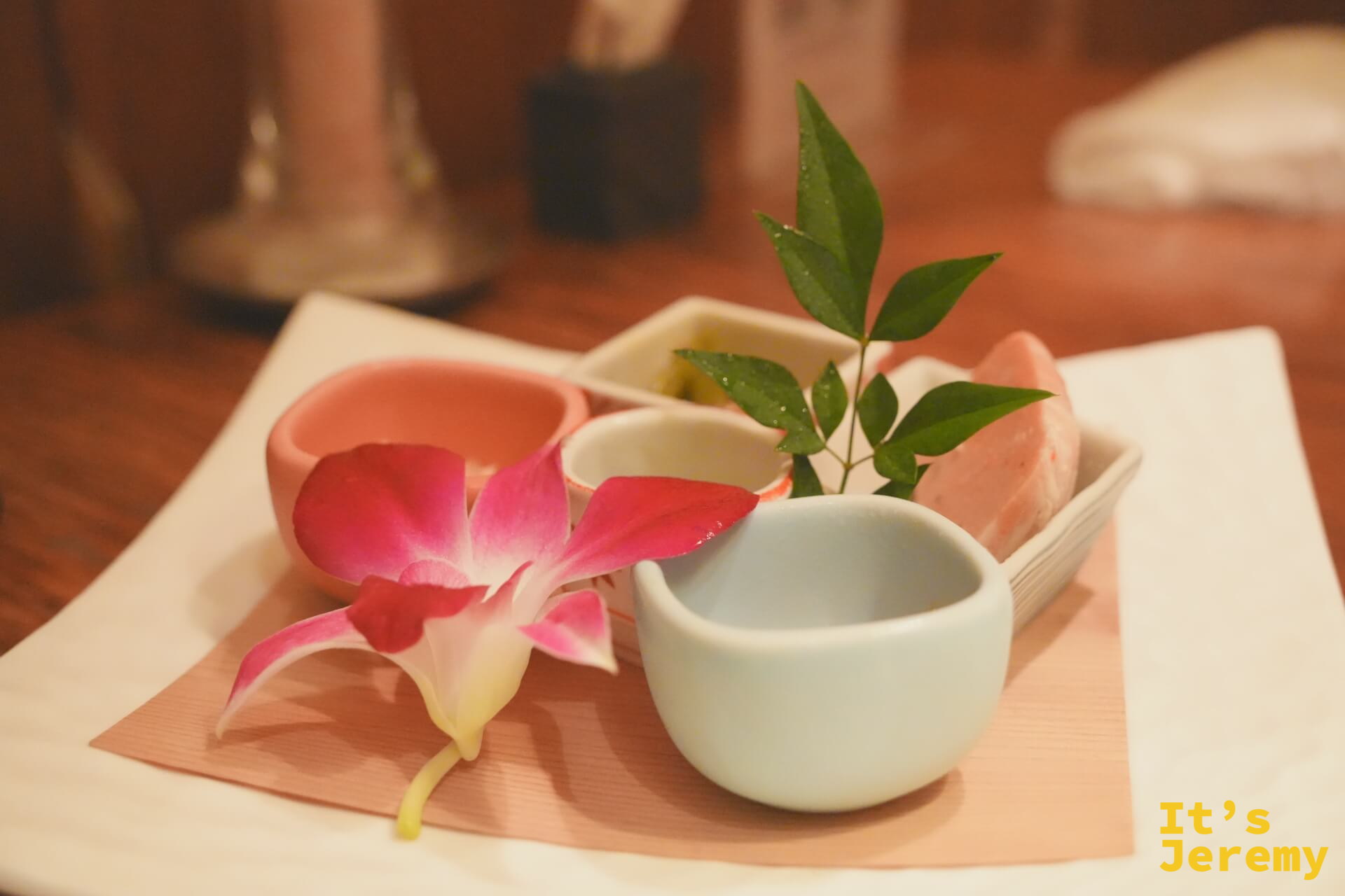 入座後送上的先付前菜,多個小陶碗排列在木托盤上,粉紅蘭花裝飾