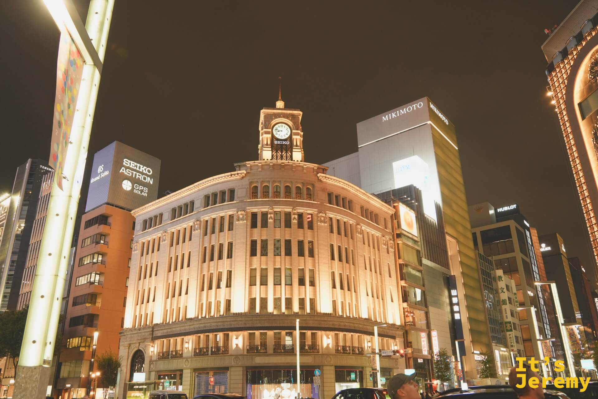 銀座夜景，和光百貨的古典鐘塔建築在夜燈下呈現暖金色，SEIKO ASTRON 和 MIKIMOTO 等招牌在周圍林立，夜空深藍