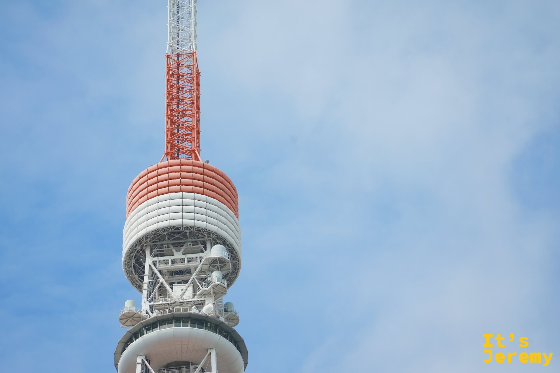 仰望東京鐵塔頂端，特別展望台的渾圓弧形構造在鐵塔最高段隱約可見，其上的廣播天線繼續向天空伸展，整體拍攝帶有明顯的仰角壓縮感
