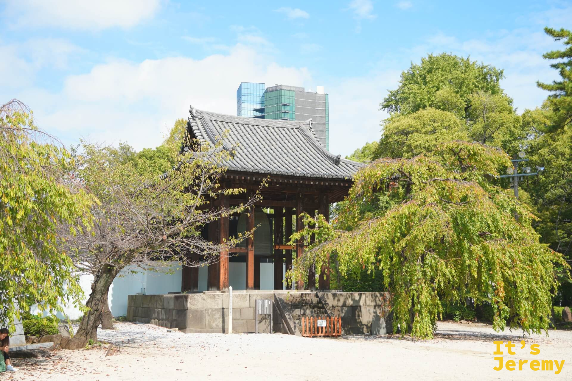 境內一隅的小型鐘亭建築,枯樹與柳樹圍繞,背後是現代建築輪廓