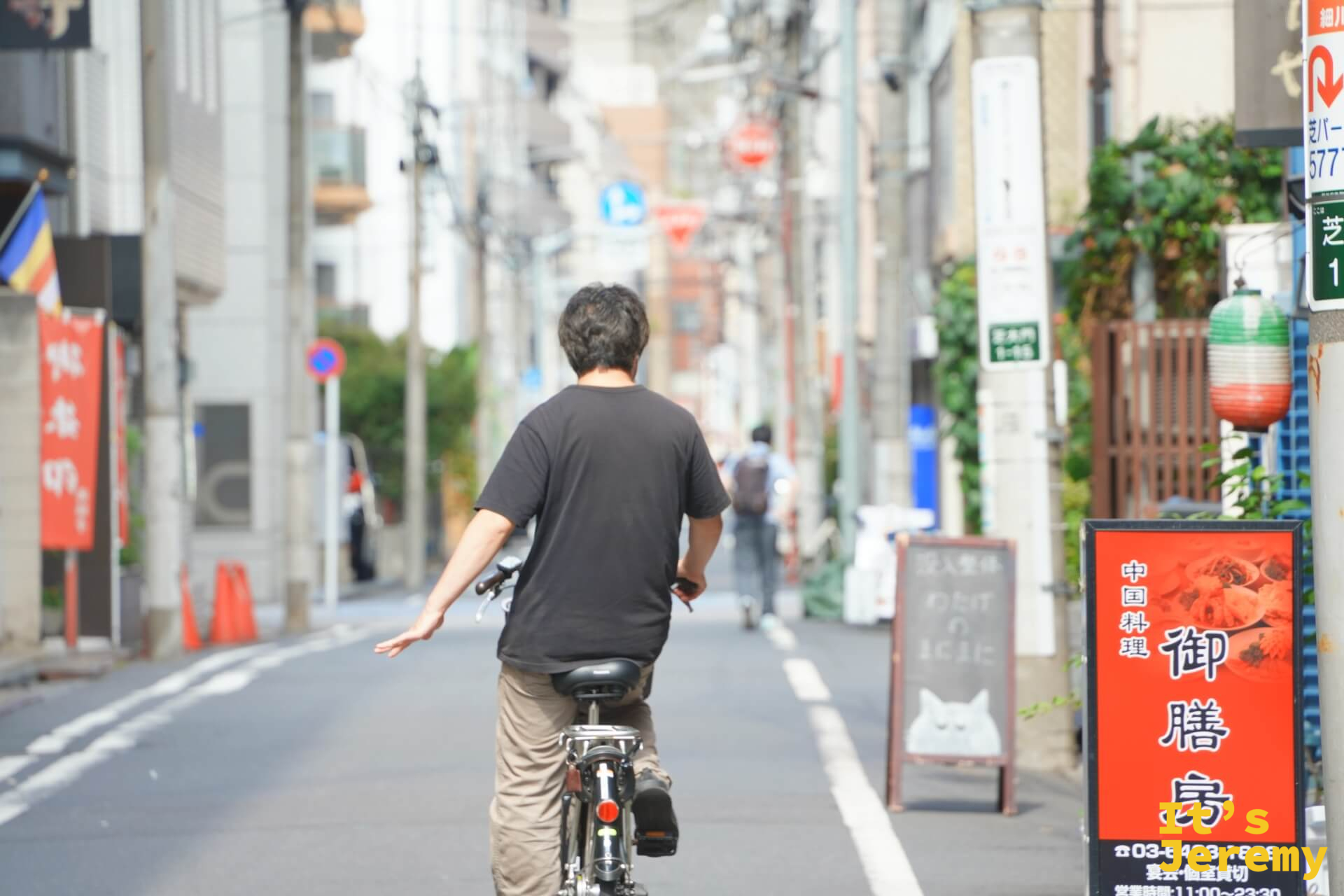 一個男人騎著腳踏車消失在港區窄巷,右側是中国料理的紅色看板,安靜的日常感