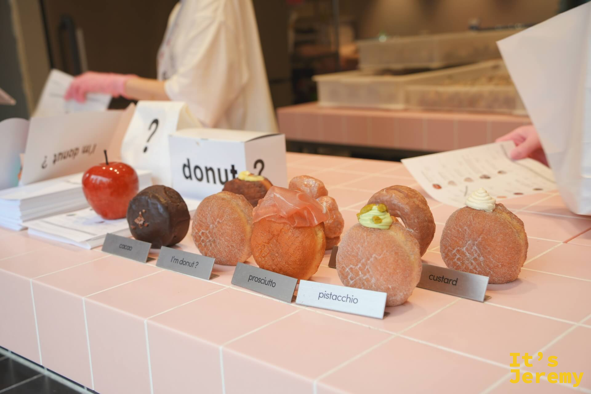 展示台上排列的各口味甜甜圈,名牌依序標示 cacao、I