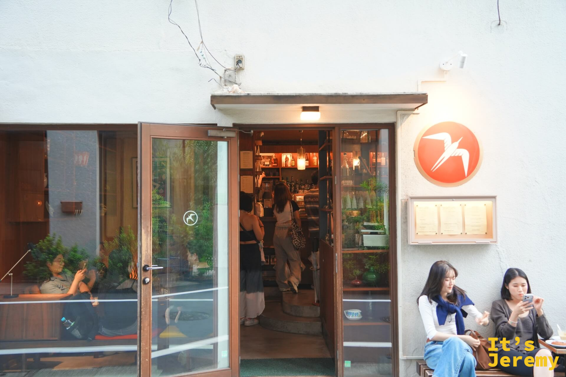 Fuglen Tokyo 入口近景,橙色燕子 logo 圓牌,玻璃門半開,裡頭一片暖黃燈光