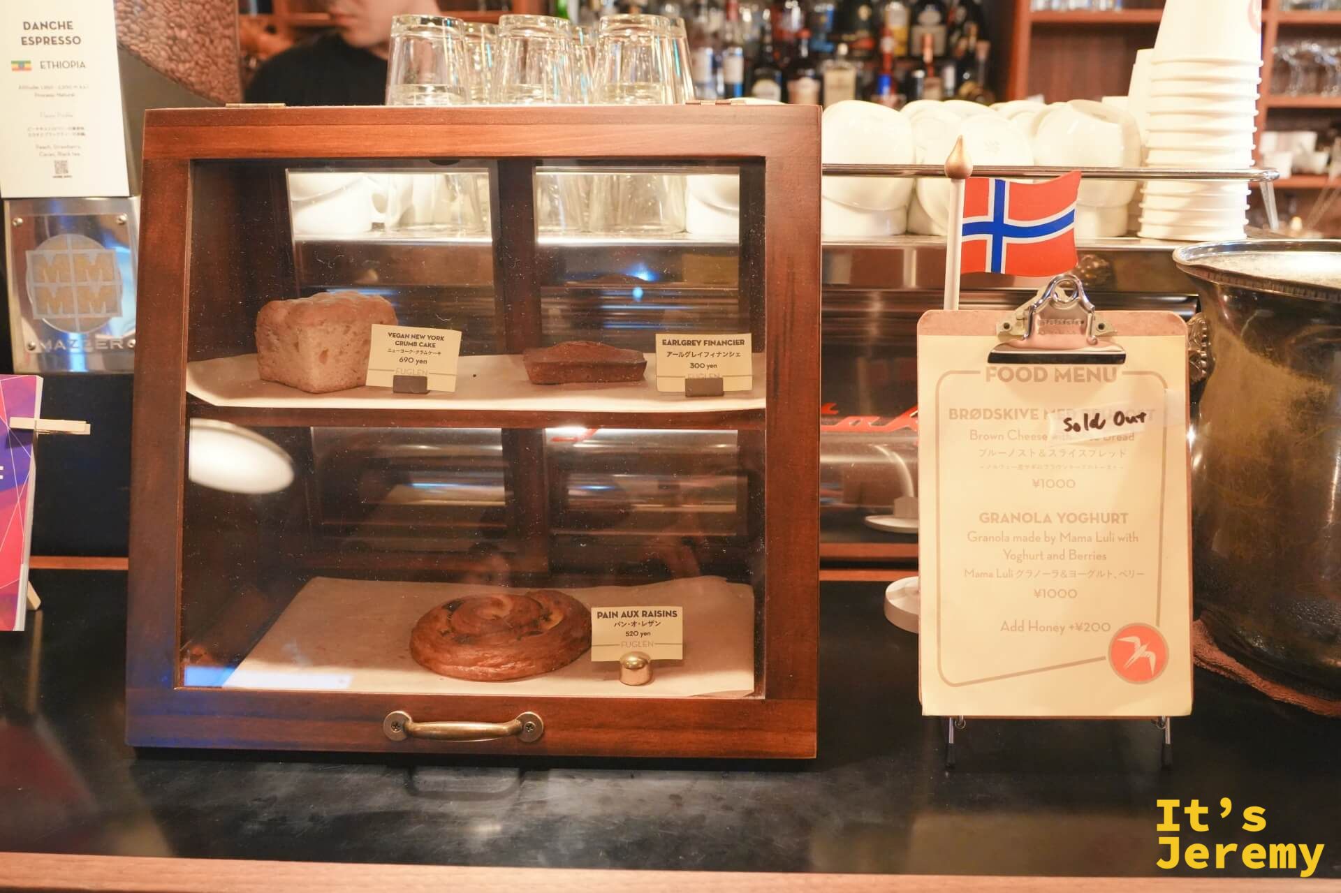 點心展示櫃:Pain aux Raisins、Earl Grey Financier、Vegan NY Crumb Cake,旁邊掛著挪威國旗和 Food Menu 看板