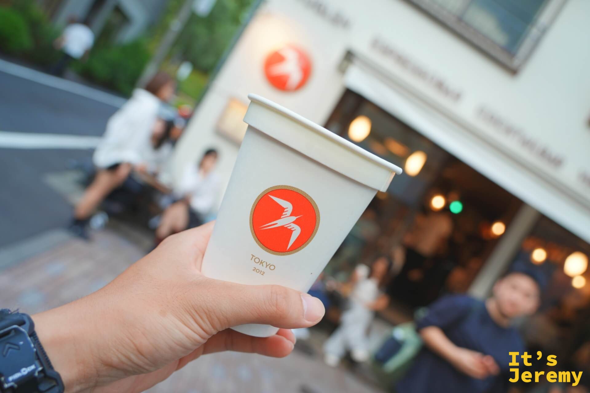 手持 Fuglen TOKYO 2012 紙杯,背景是店門外的長椅與暖黃燈光